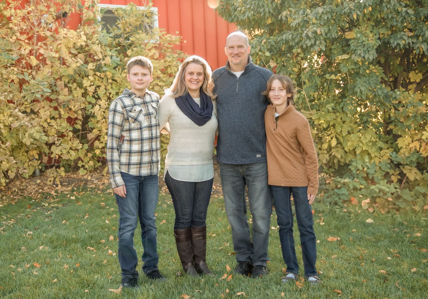 A family group poses together outdoors in coordinating casual outfits against a fall backdrop.