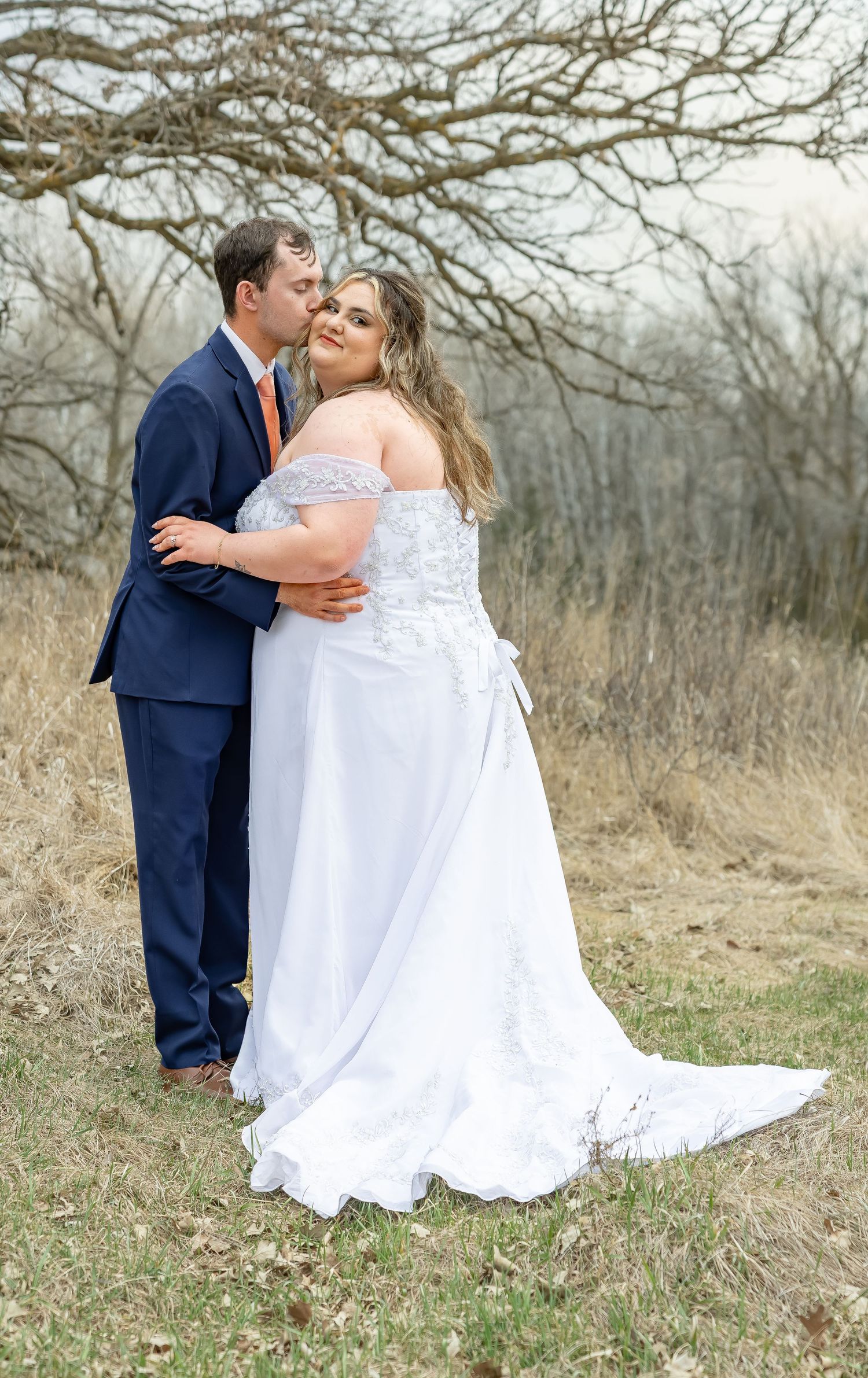 Romantic wedding couple portraits in a field with bare winter trees in the background.