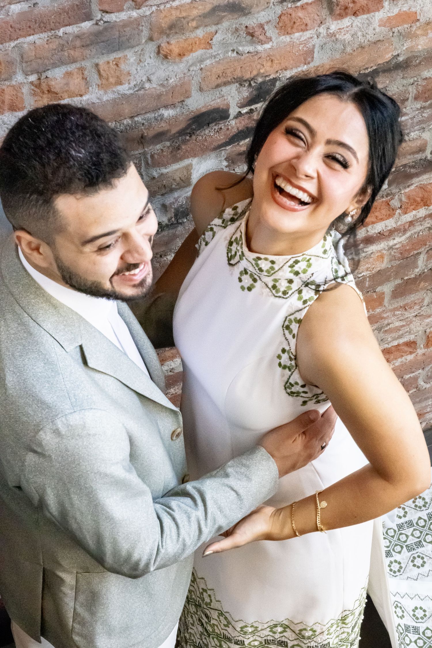 A couple shares a joyful moment together against a rustic brick wall backdrop.
