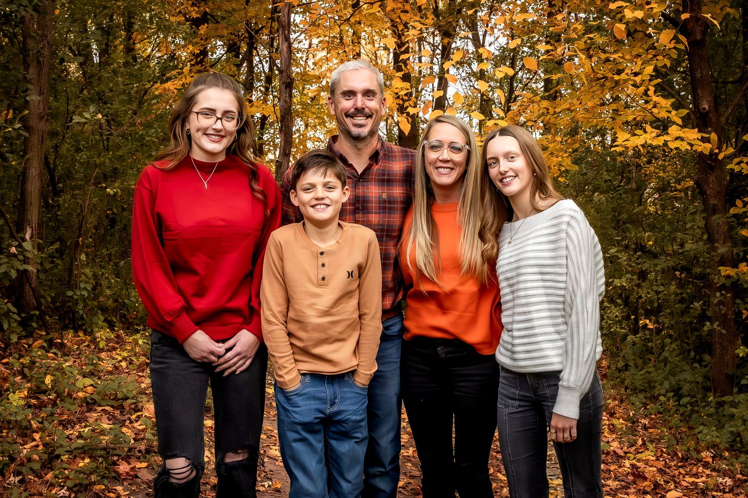 Family group portrait with autumn foliage and trees in background.