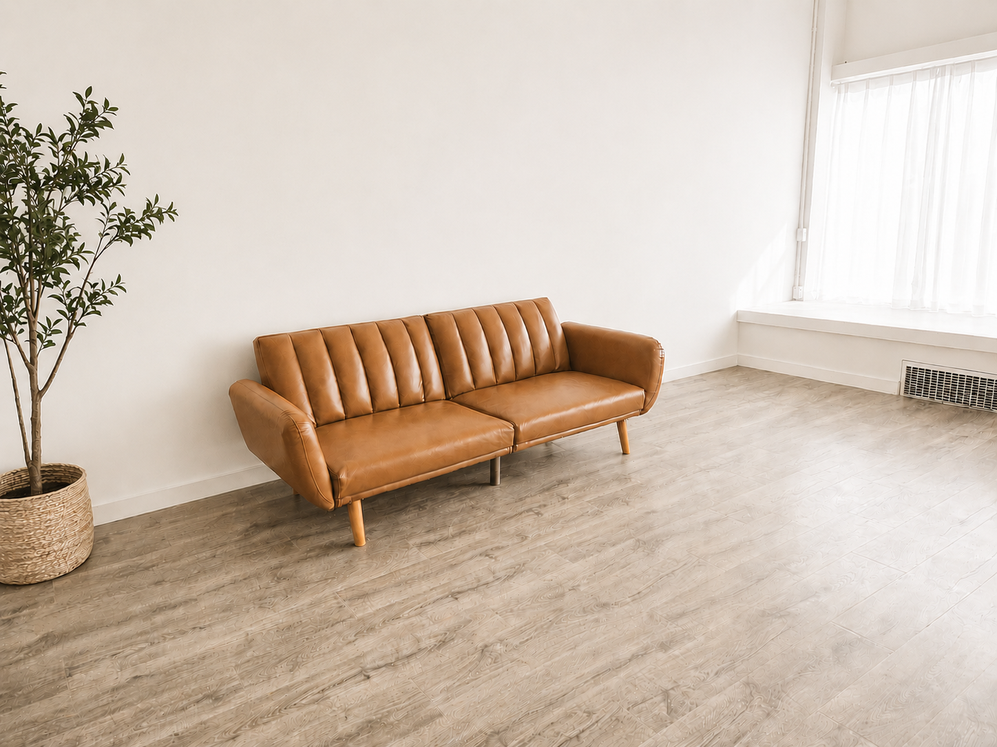 A mid-century modern tan leather sofa with channel tufting and wooden legs on light hardwood floors beside a potted olive tree.