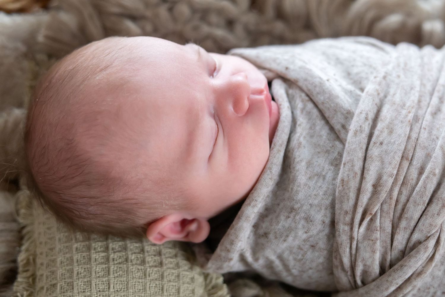 Close-up view of a sleeping baby in a gray outfit lying on white bedding.