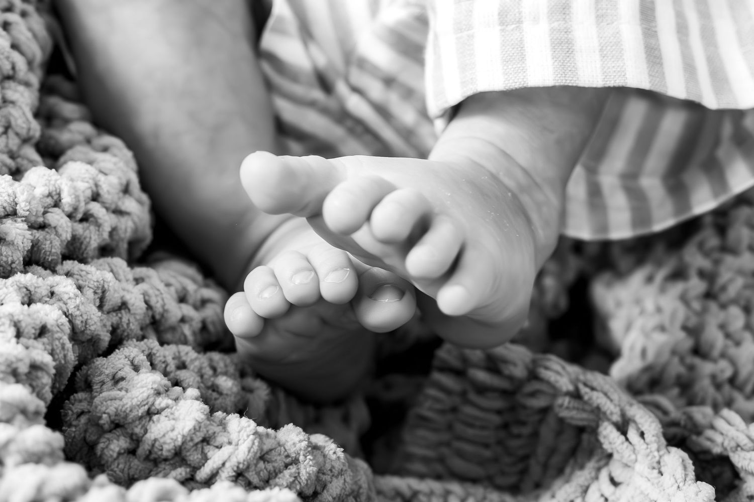 Close-up black and white photo of tiny baby feet resting on knitted blanket.