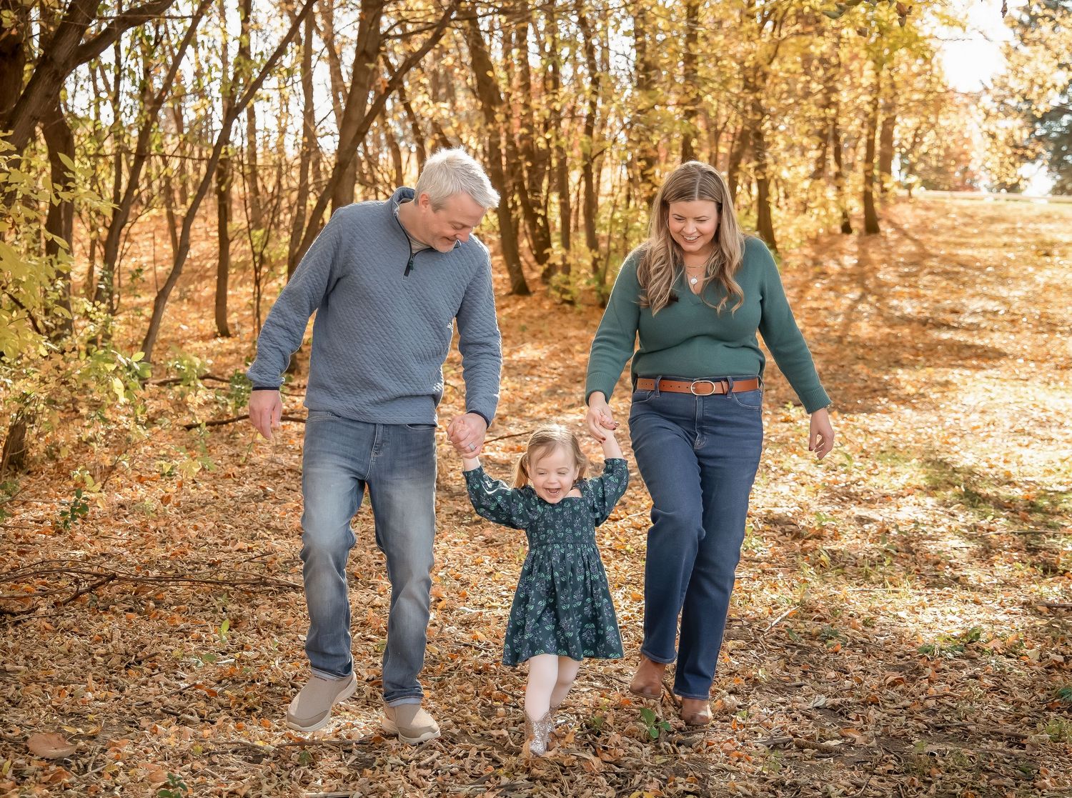 Family members' legs and feet are shown walking together on a woodland path in autumn.