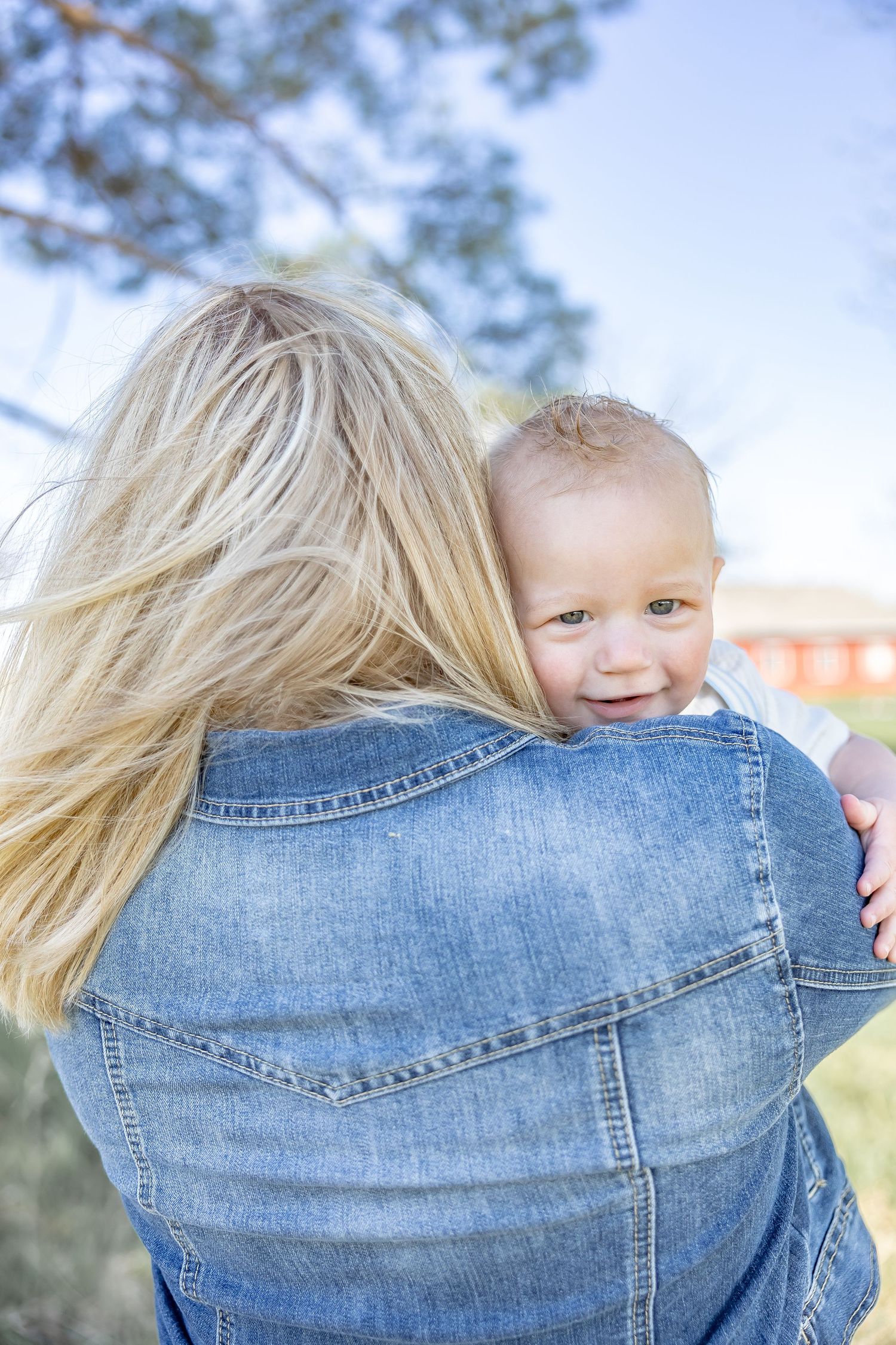 Close-up series showing back of denim jacket while holding small child outdoors.