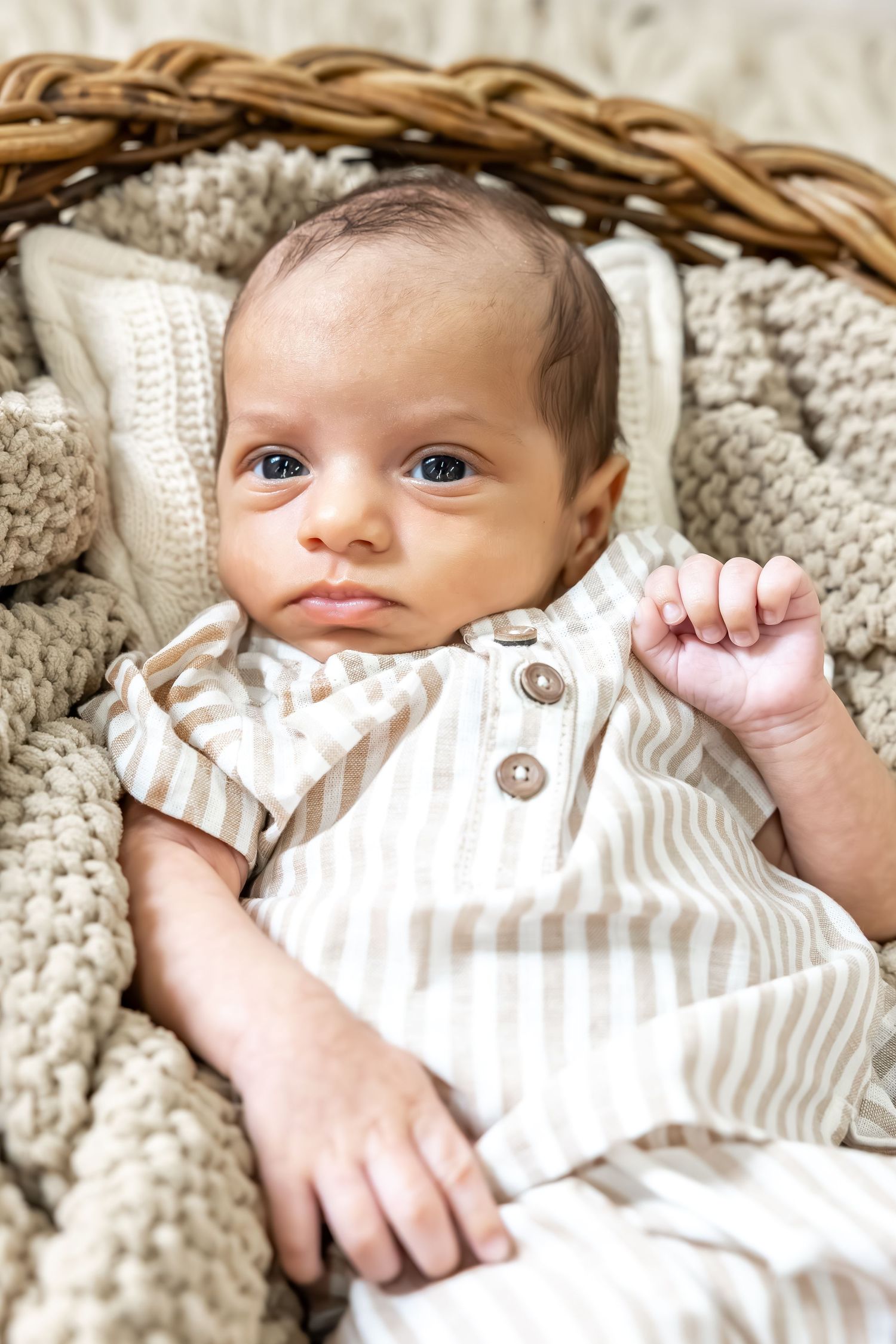 Baby in striped outfit resting on knitted blanket in woven basket.