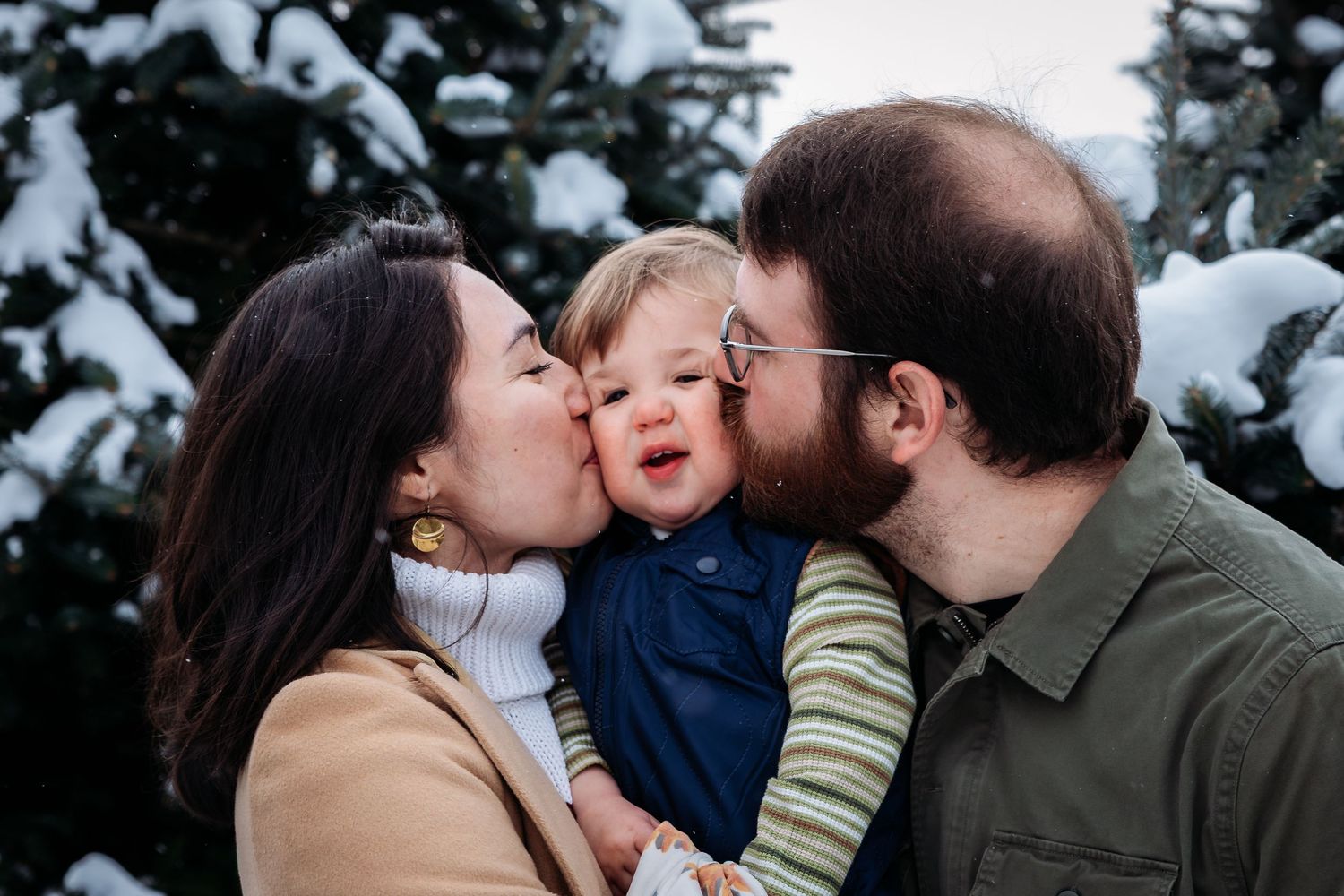 Intimate family moment shared with kisses among snow-covered pine trees.