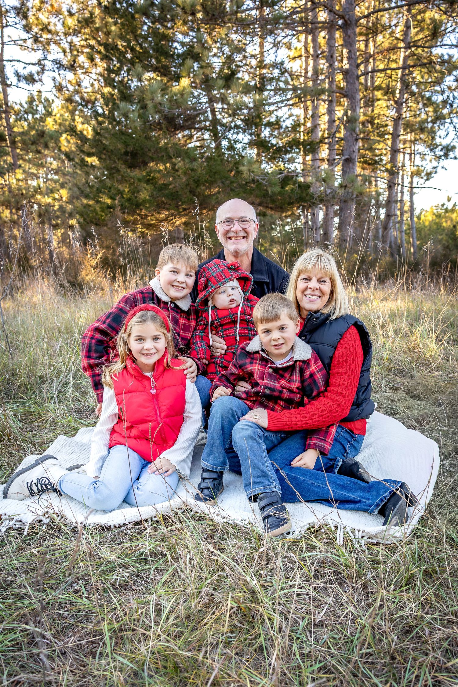 Group relaxing on white blanket in wooded area wearing coordinated red plaid and denim outfits.
