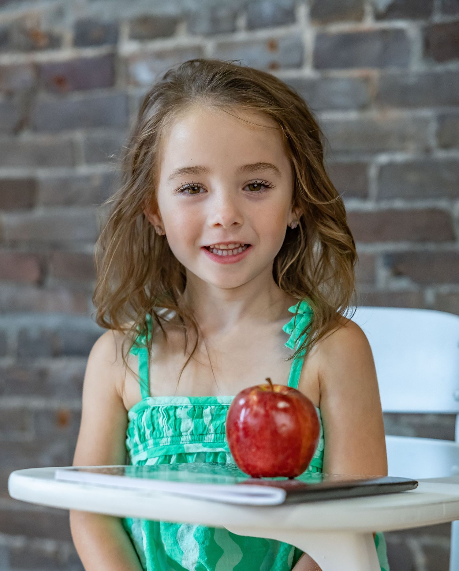 A bright red apple sits on a white table next to someone wearing a mint green summer dress.
