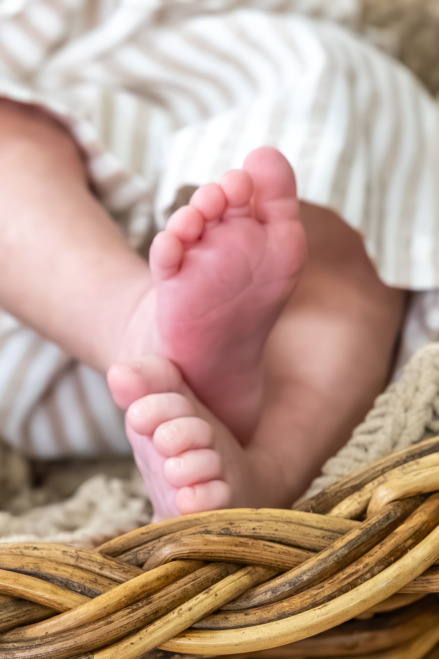 Tiny baby feet rest on woven basket material in soft natural lighting.