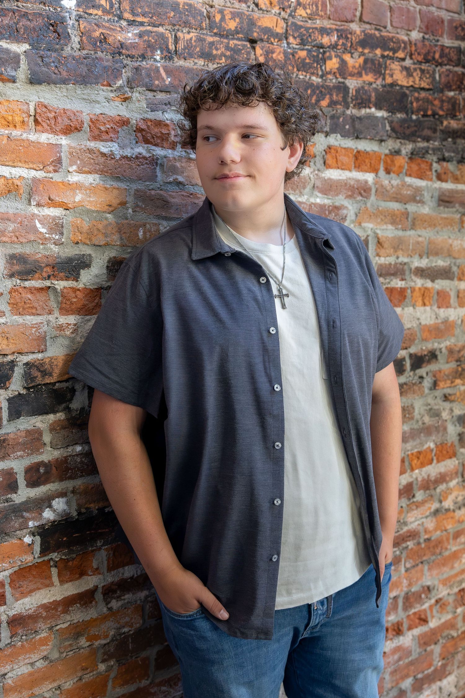Casual portrait against brick wall wearing gray button-down shirt and jeans.