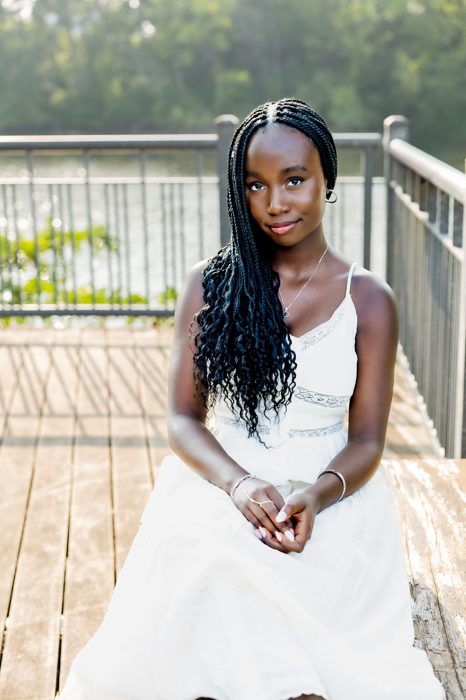 A person in a white dress poses elegantly on a wooden deck during a summer photo session.
