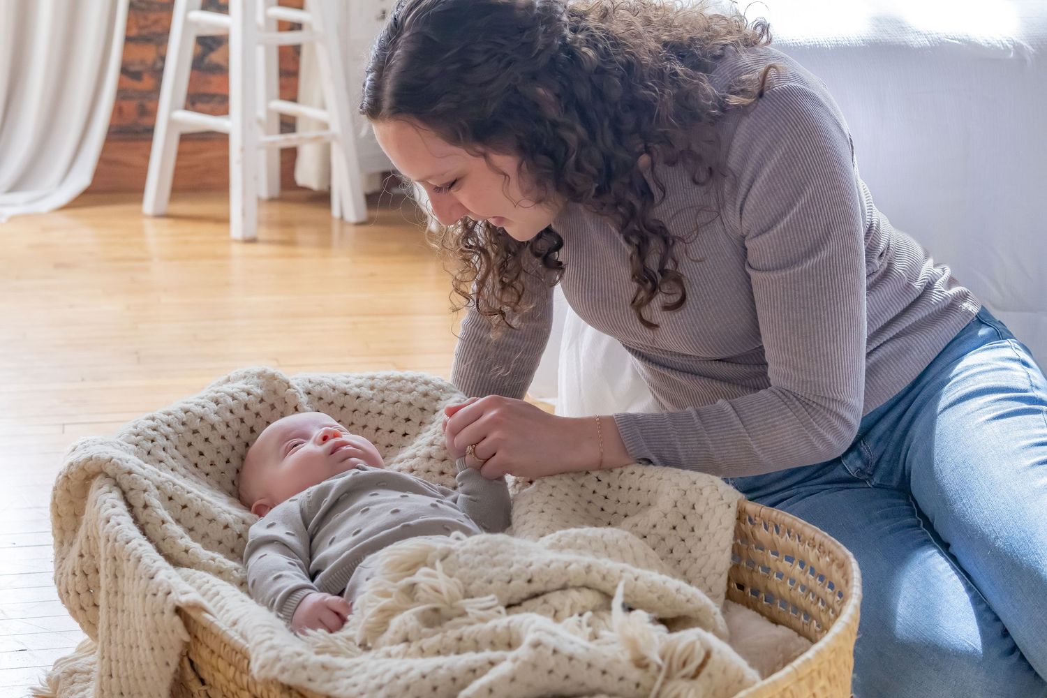 Parent leaning over a woven basket containing a baby wrapped in a knit blanket.