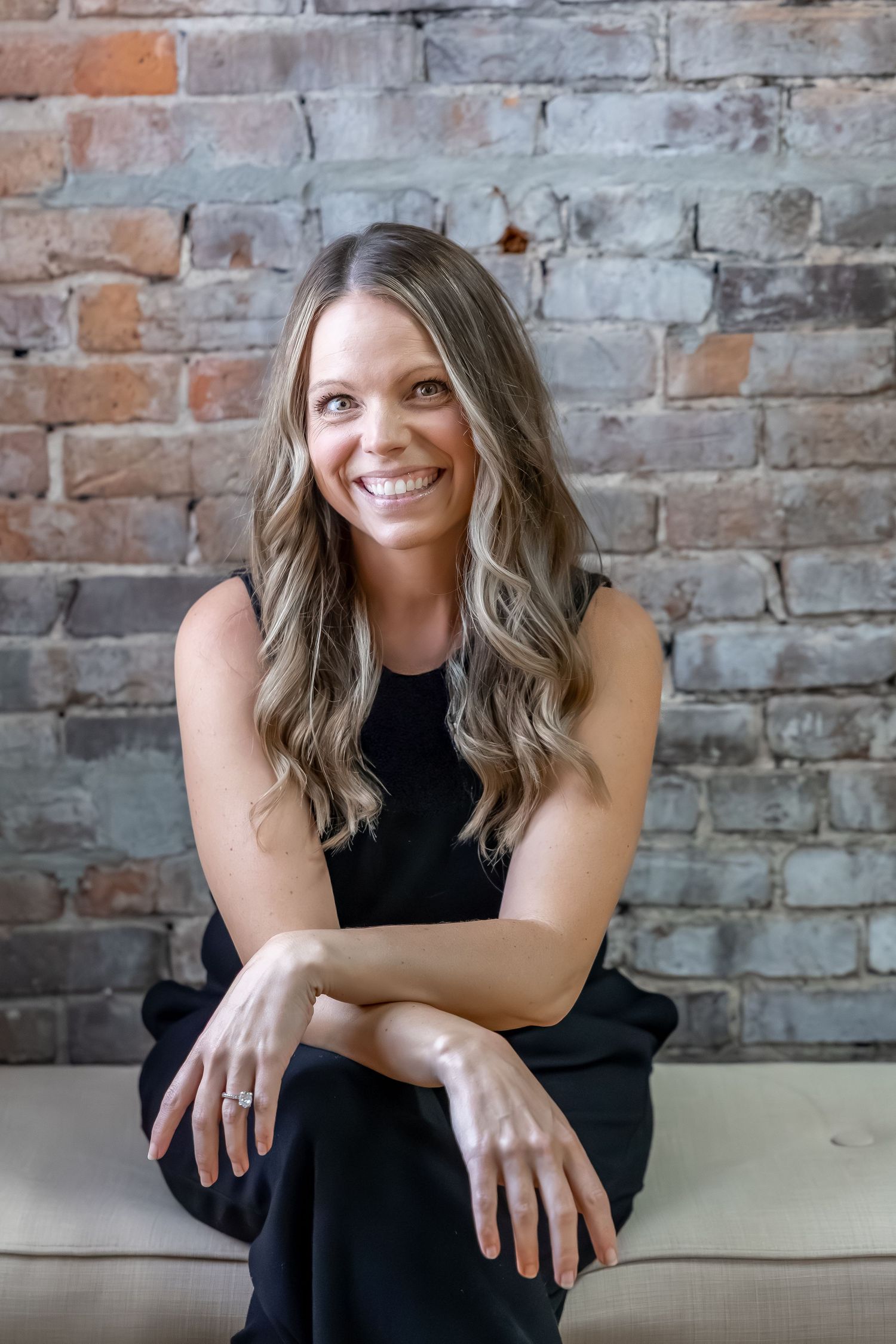Portrait series of photographer in black dress against rustic brick wall.