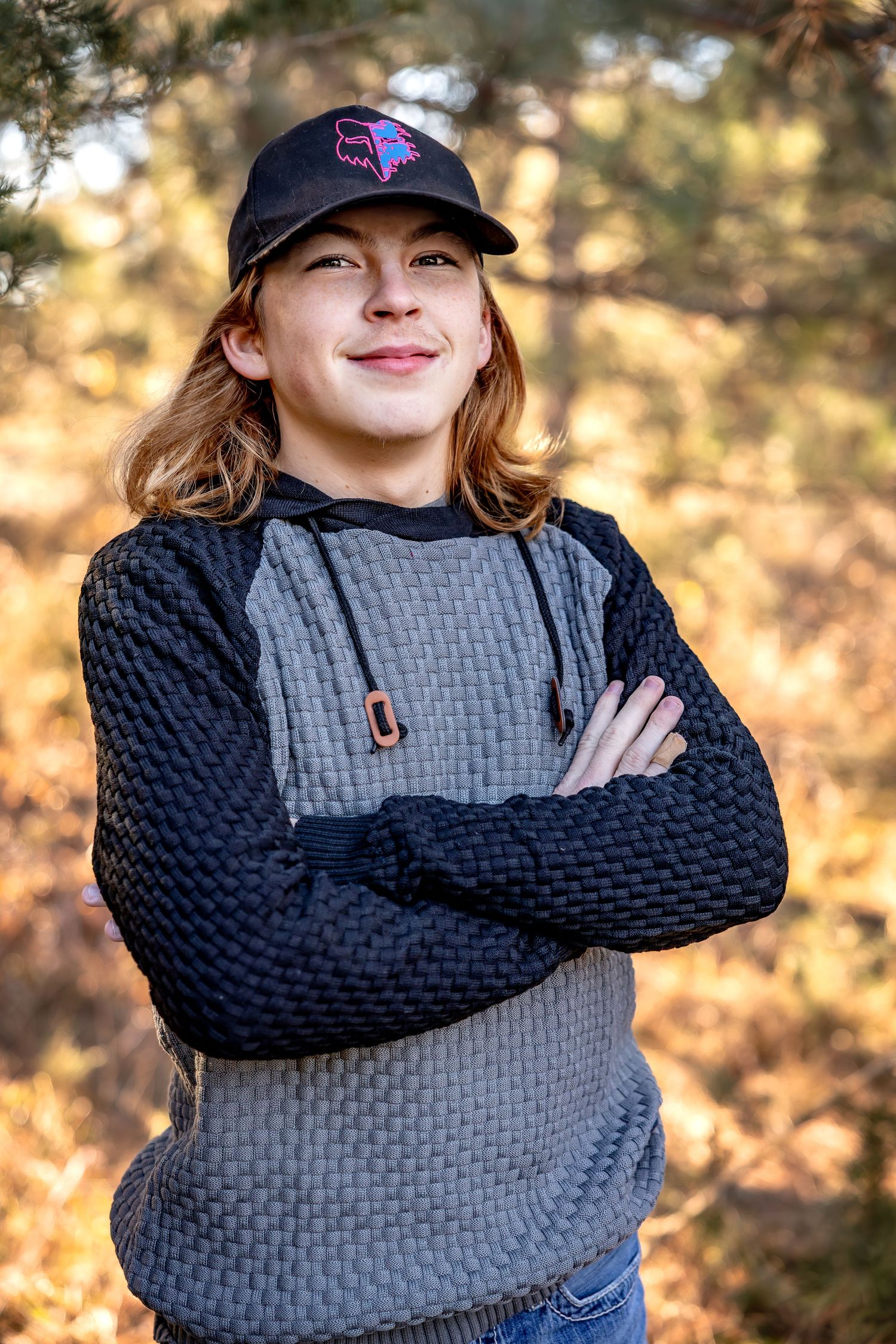 Casual portrait series in a grey sweater with navy sleeves and baseball cap against autumn foliage.