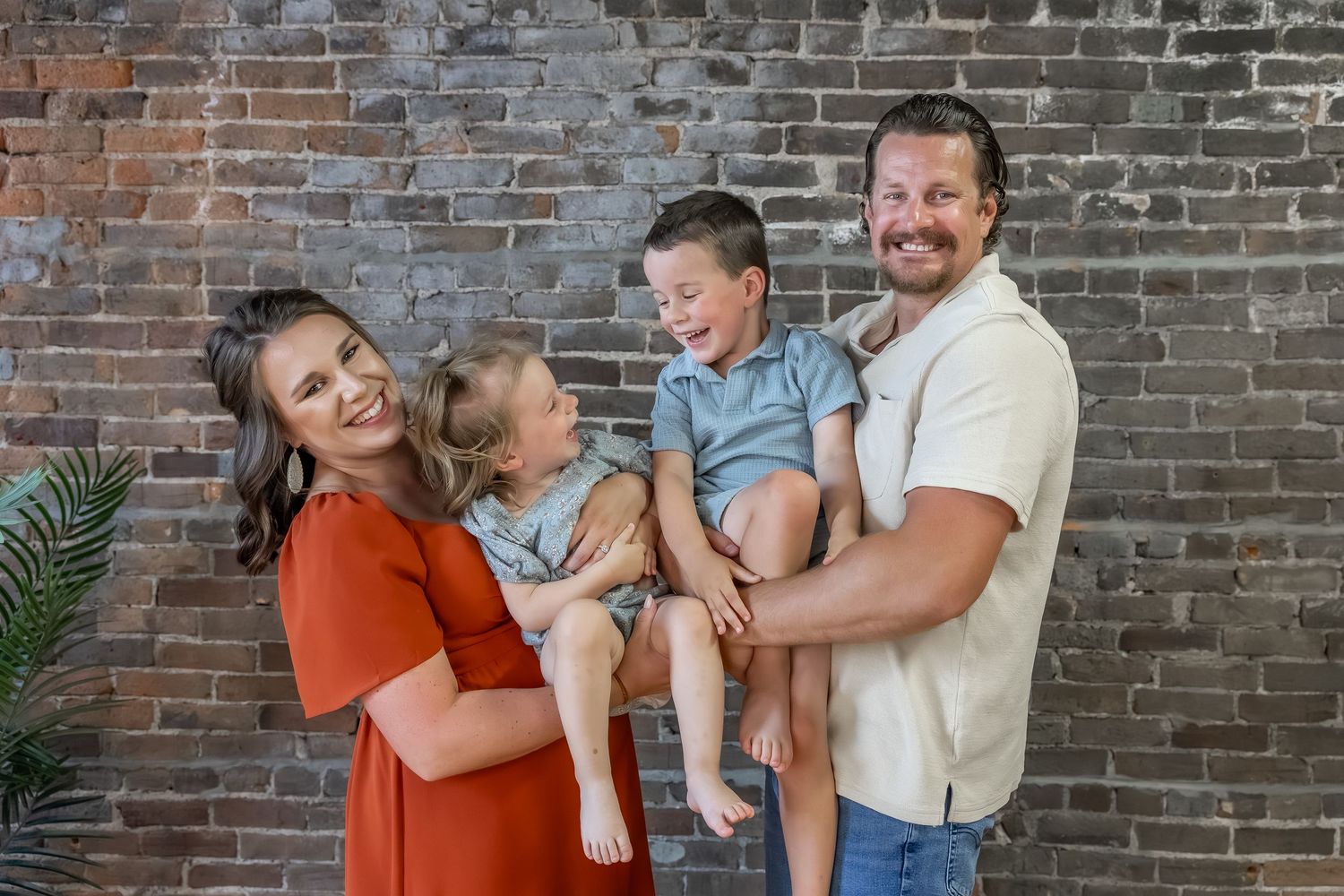 Candid family portrait session with joyful expressions against brick wall.