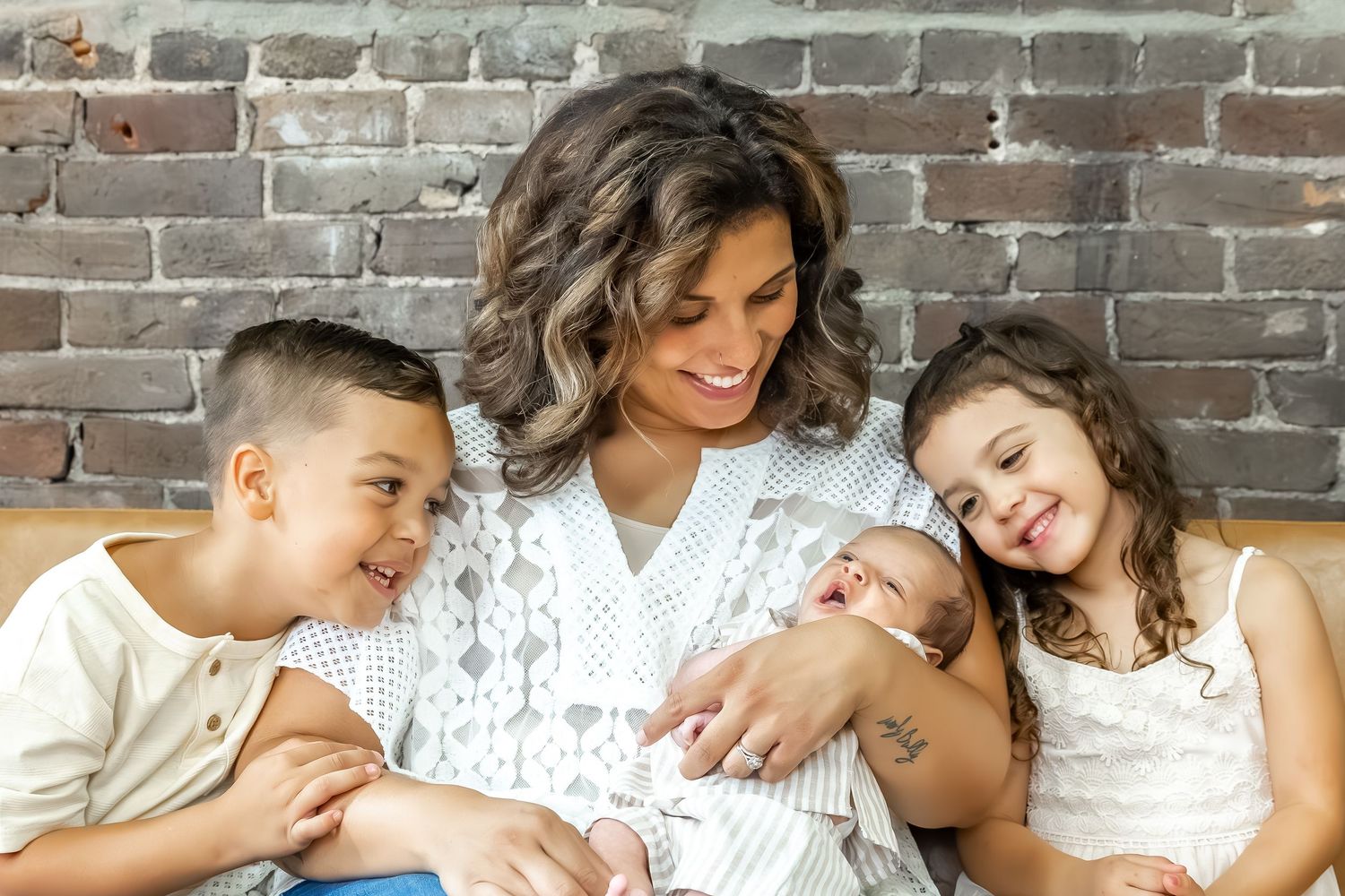 Family relaxing together on brown leather couch against exposed brick wall.