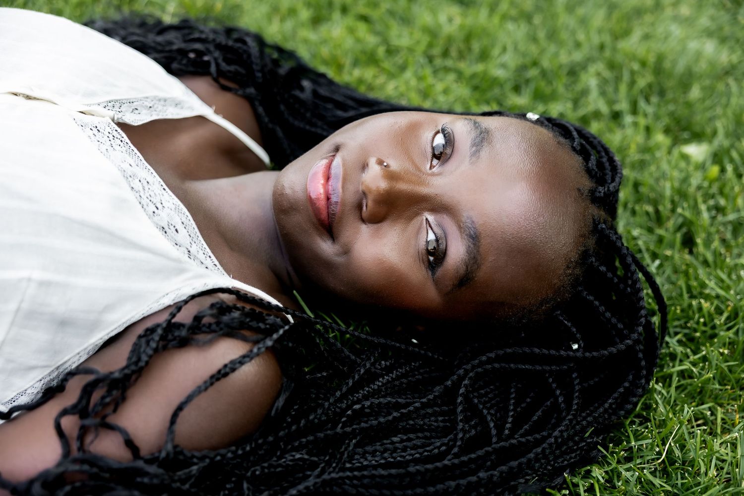 A person with braided hair lies on green grass during an outdoor photo session.