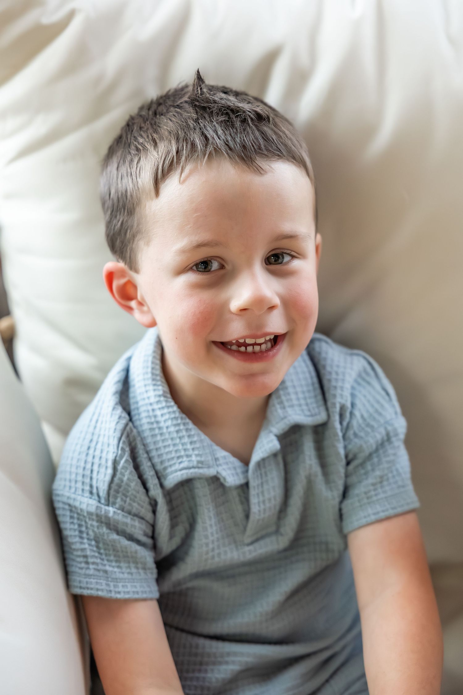 A child in a light blue polo shirt smiles while resting on white cushions.