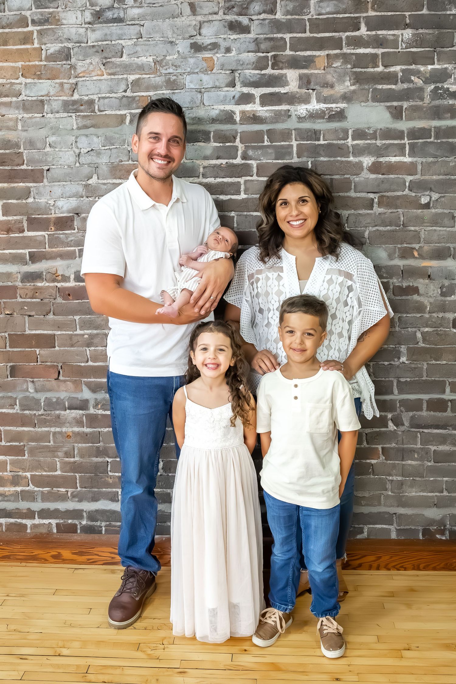 Modern family photo session with urban brick wall and hardwood floor setting.