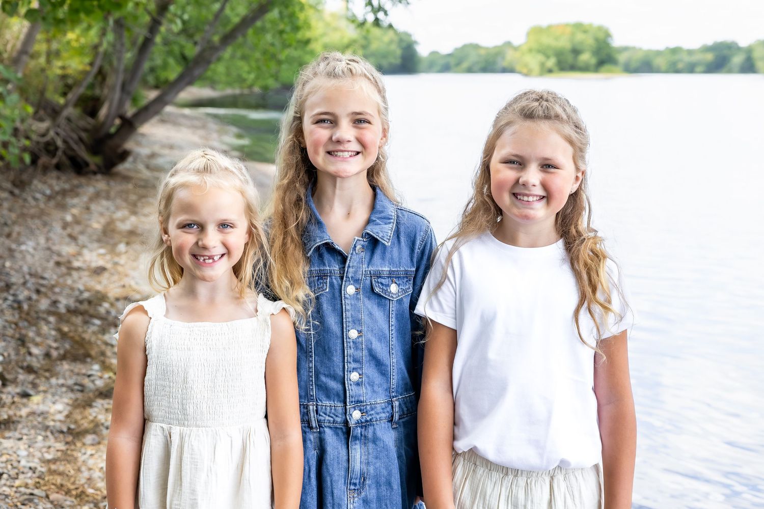 Three children sitting together on a bench near a lake on a sunny summer day.