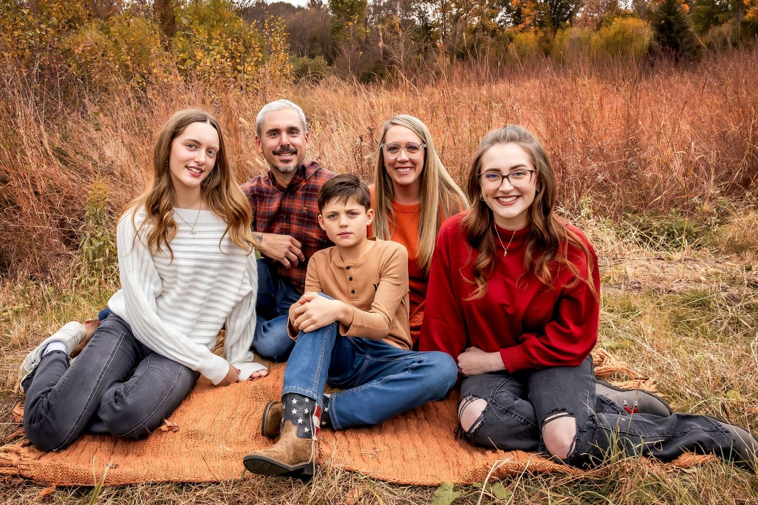 A casual family portrait taken outdoors in a field with golden autumn colors in the background.