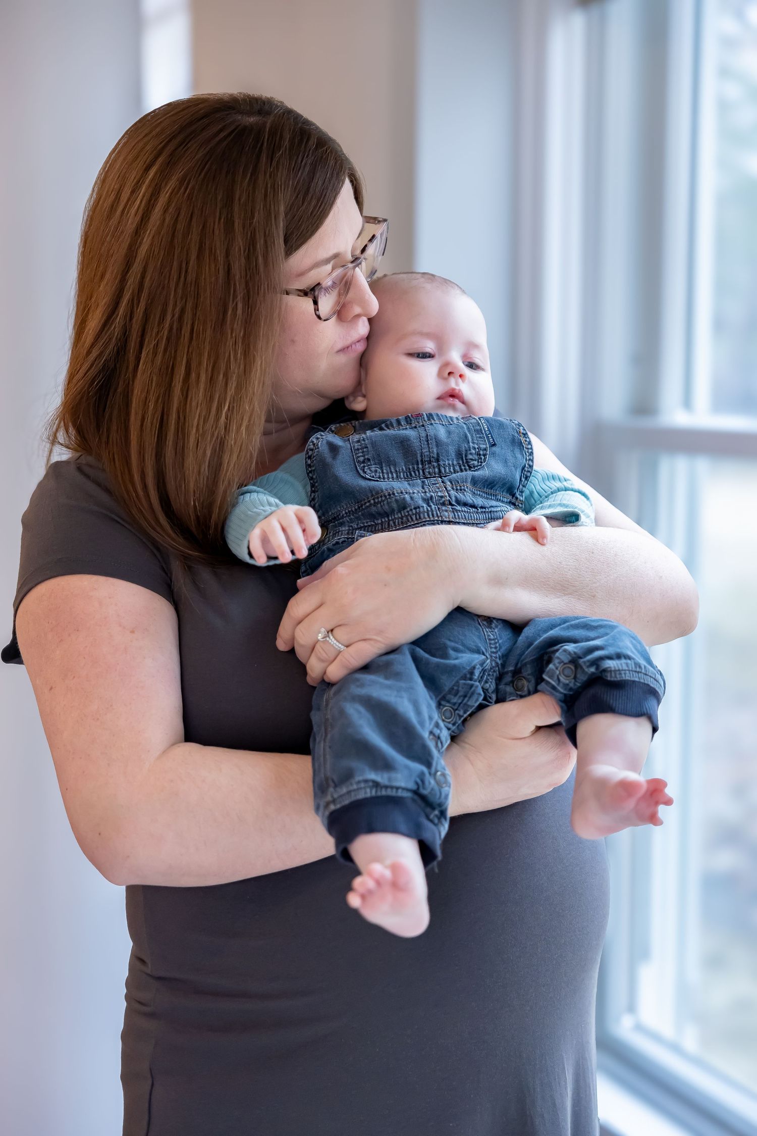 Tender moment between parent and infant by window in natural light portrait.