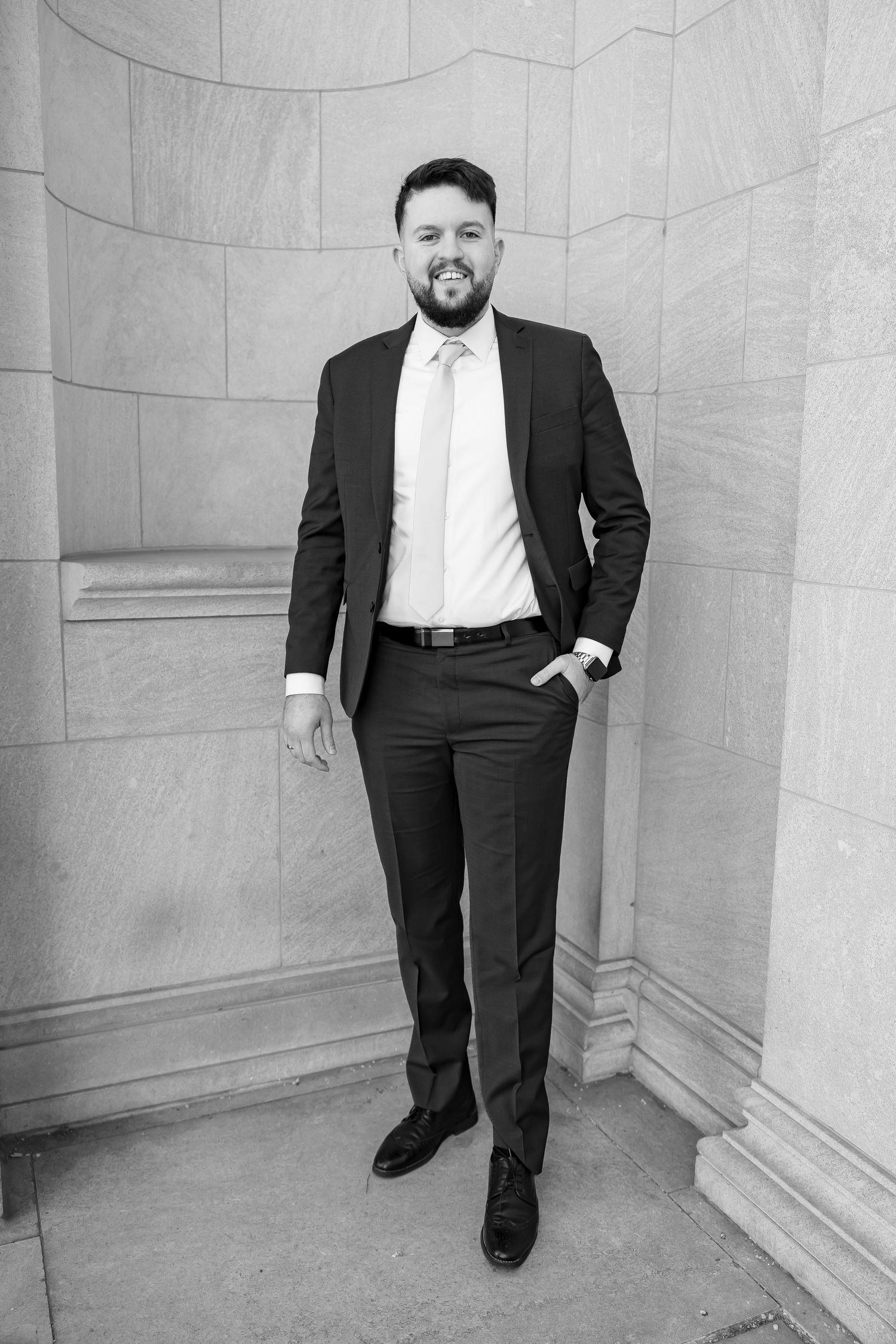 Black and white portraits of a groom in a classic suit posing against a stone wall.