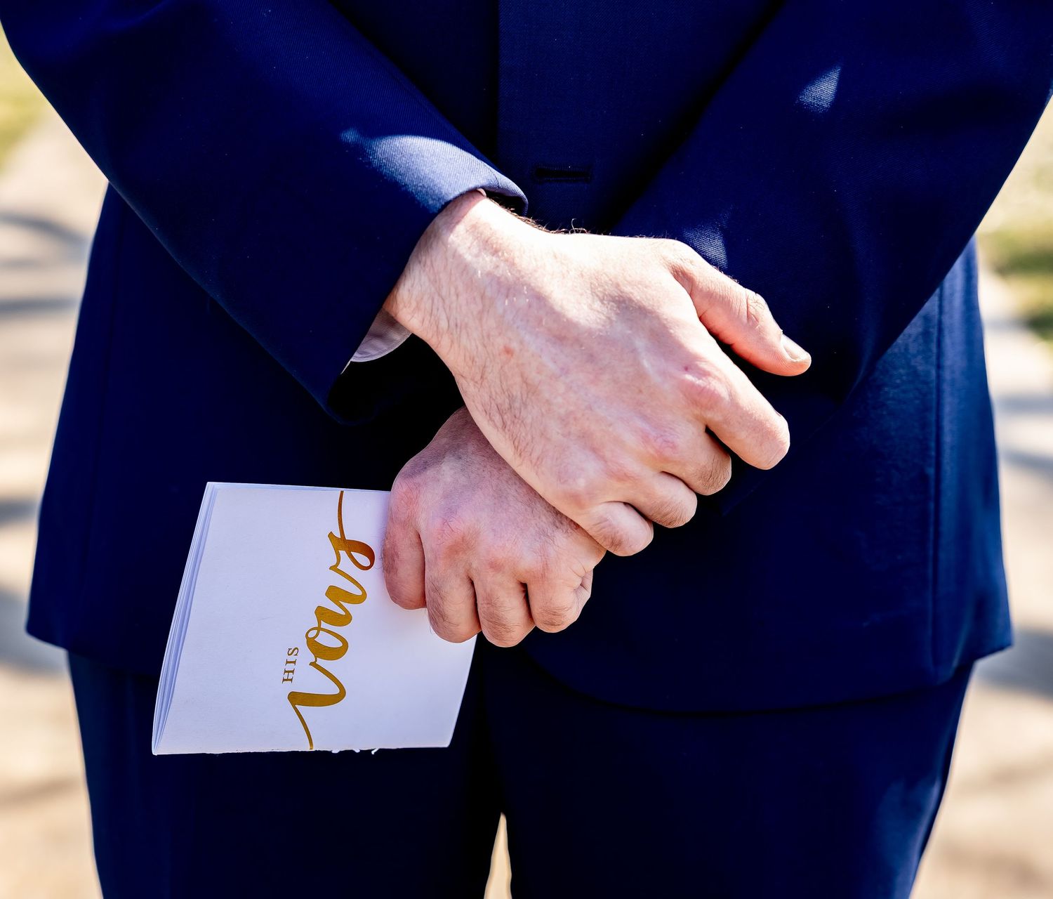 A close-up of hands holding wedding programs in navy blue and white during an outdoor ceremony.