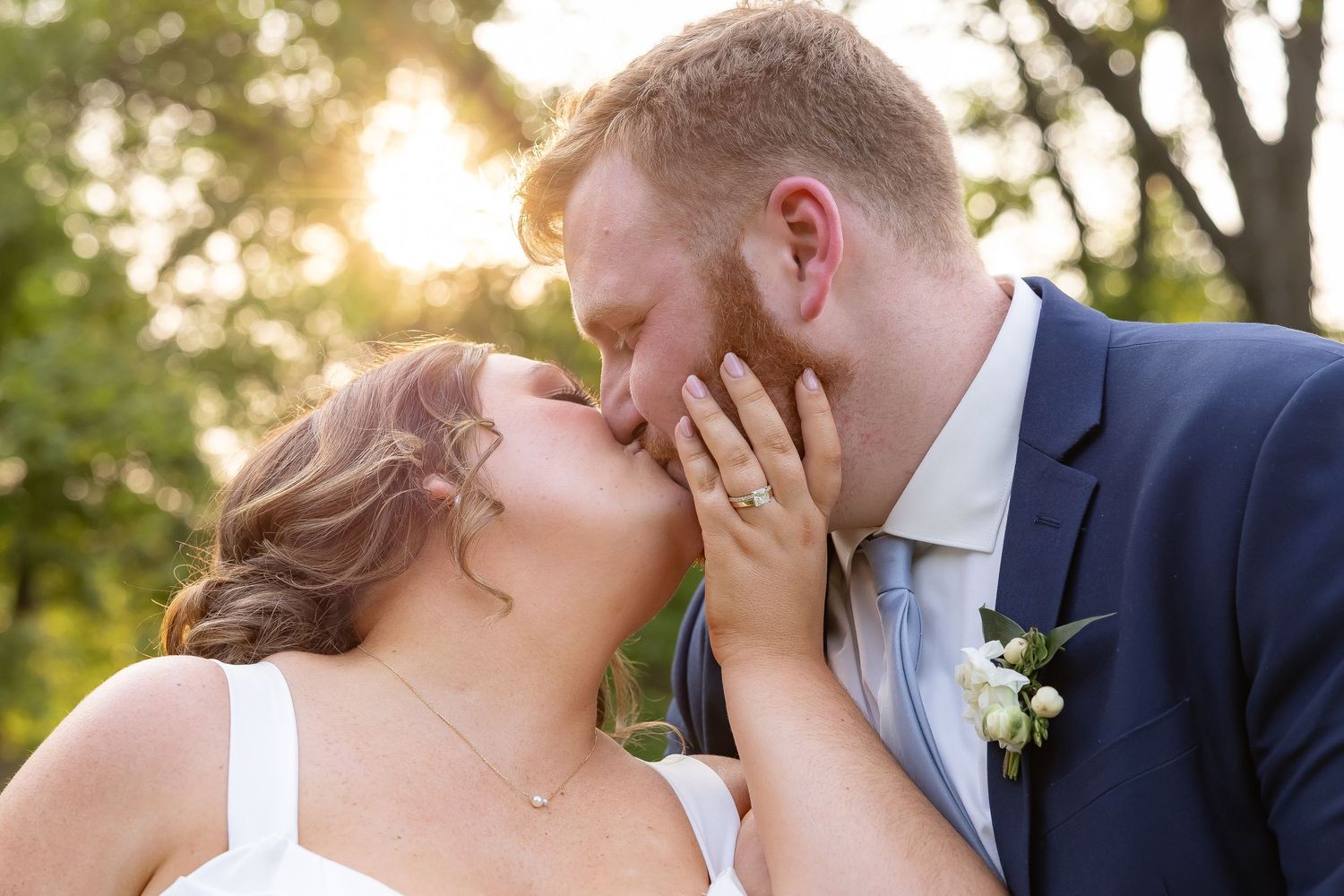 Romantic sunset wedding portrait shows tender moment between newlyweds in natural outdoor setting.