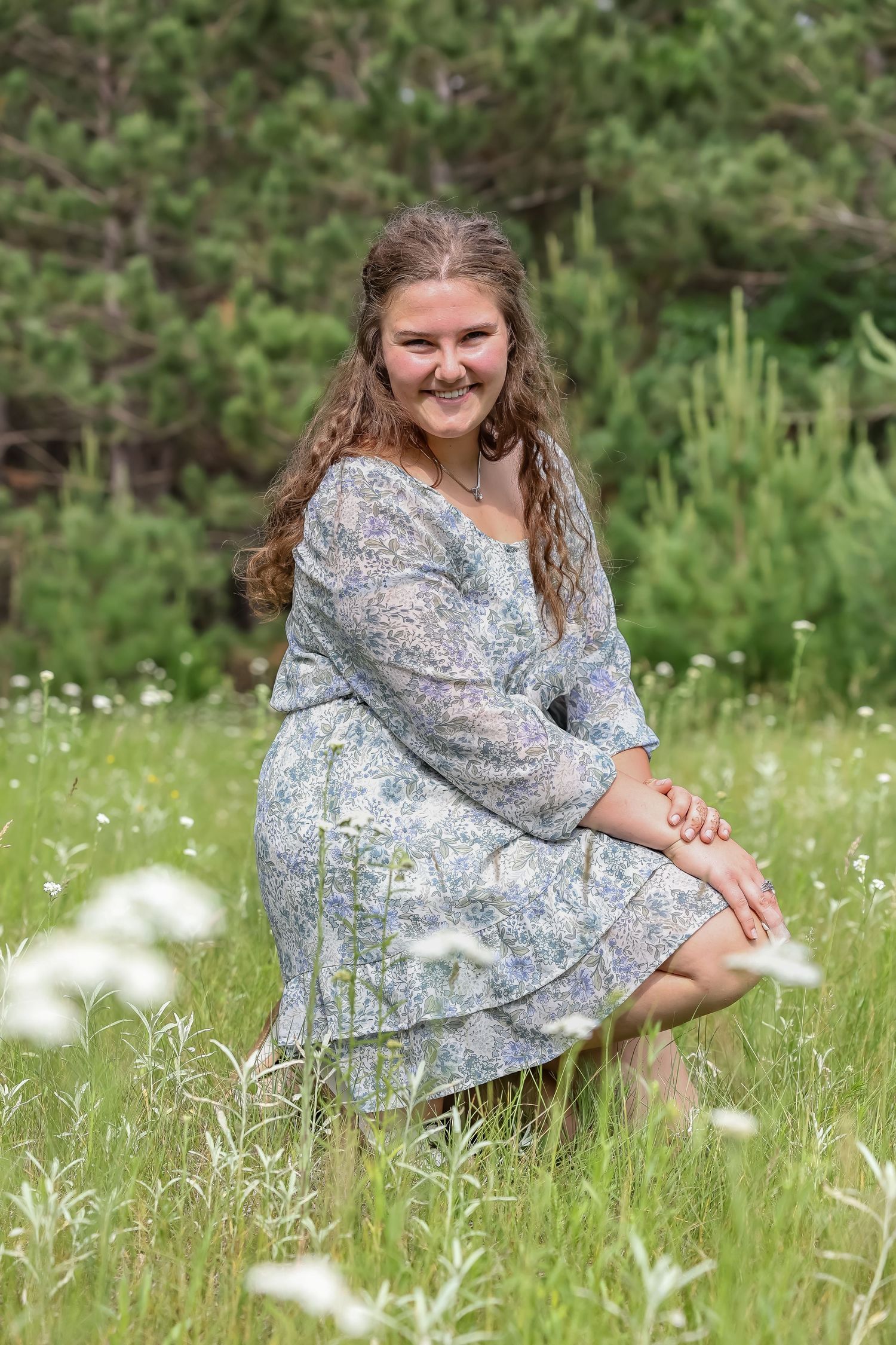 Dreamy portraits of someone in a floral dress sitting in a wildflower meadow.