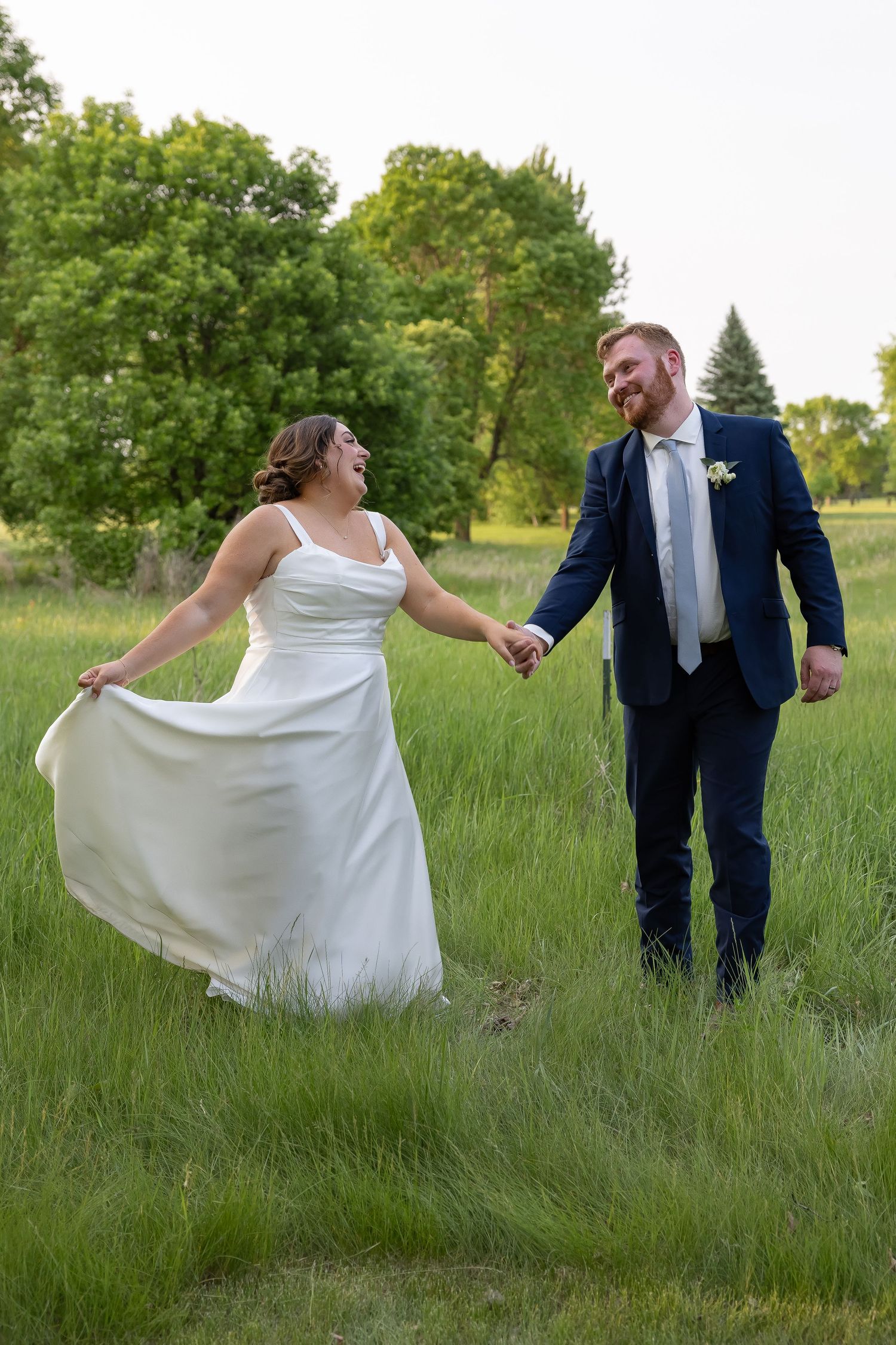 Playful newlyweds dance and twirl in a grassy field during their wedding photoshoot.