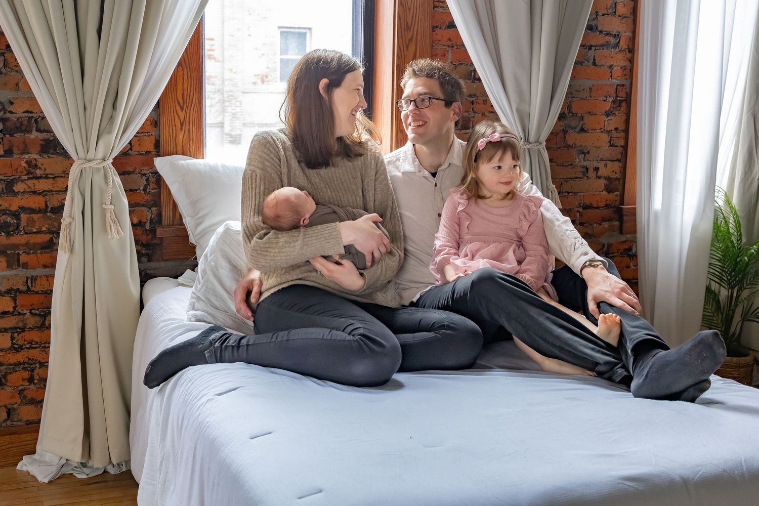 Family lounges together on bed during casual lifestyle photoshoot in industrial style room.
