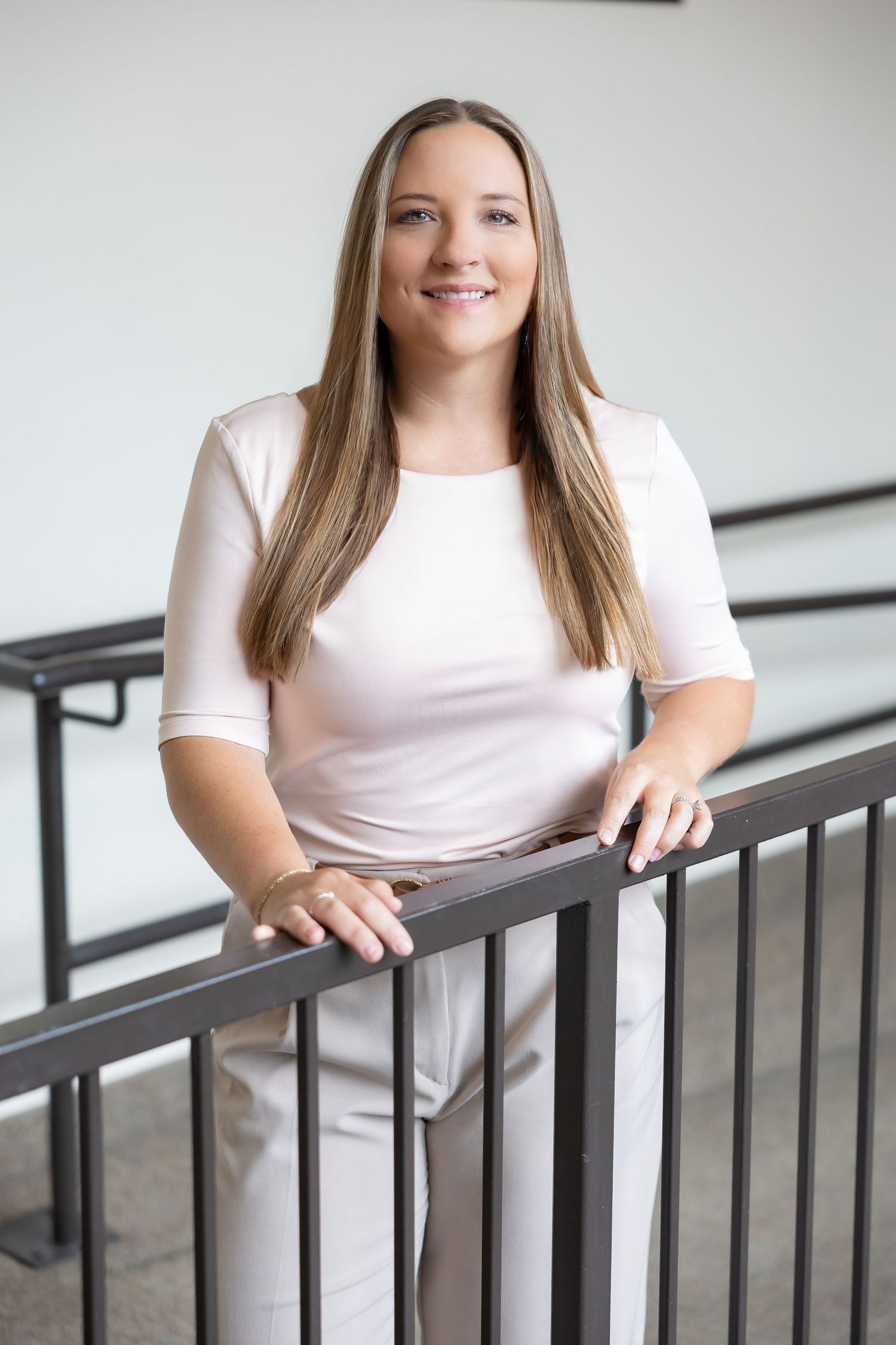 Portrait of person in white top leaning on railing in bright indoor setting.