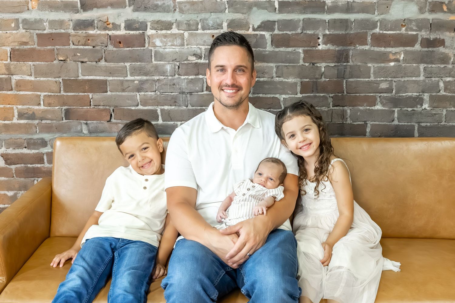 Family group photo on leather couch with exposed brick wall background.