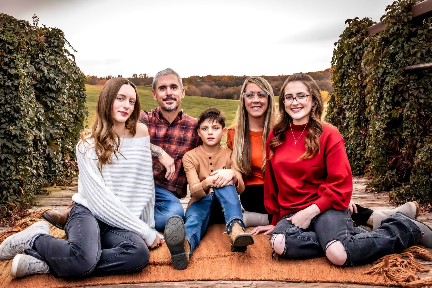 A family sits together on a wooden platform surrounded by autumn foliage for an outdoor portrait session.
