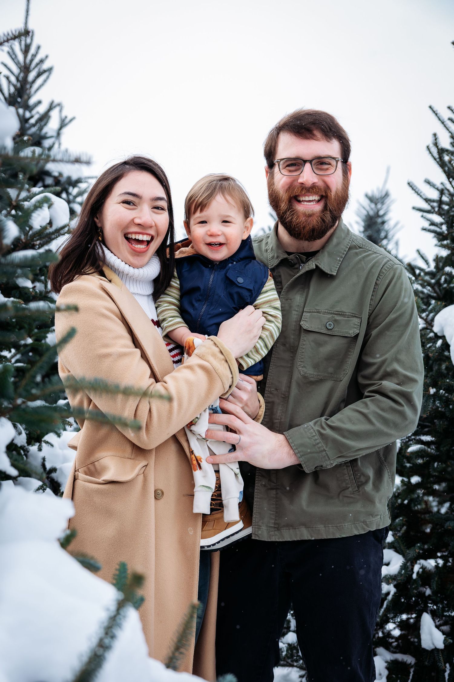 Joyful family portrait captured in snowy forest setting with evergreen trees.