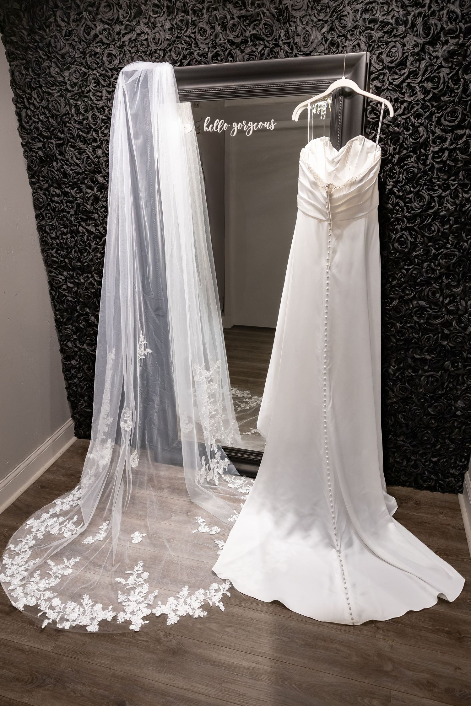 a white wedding dress with a delicate lace veil displayed against a dark patterned wall.