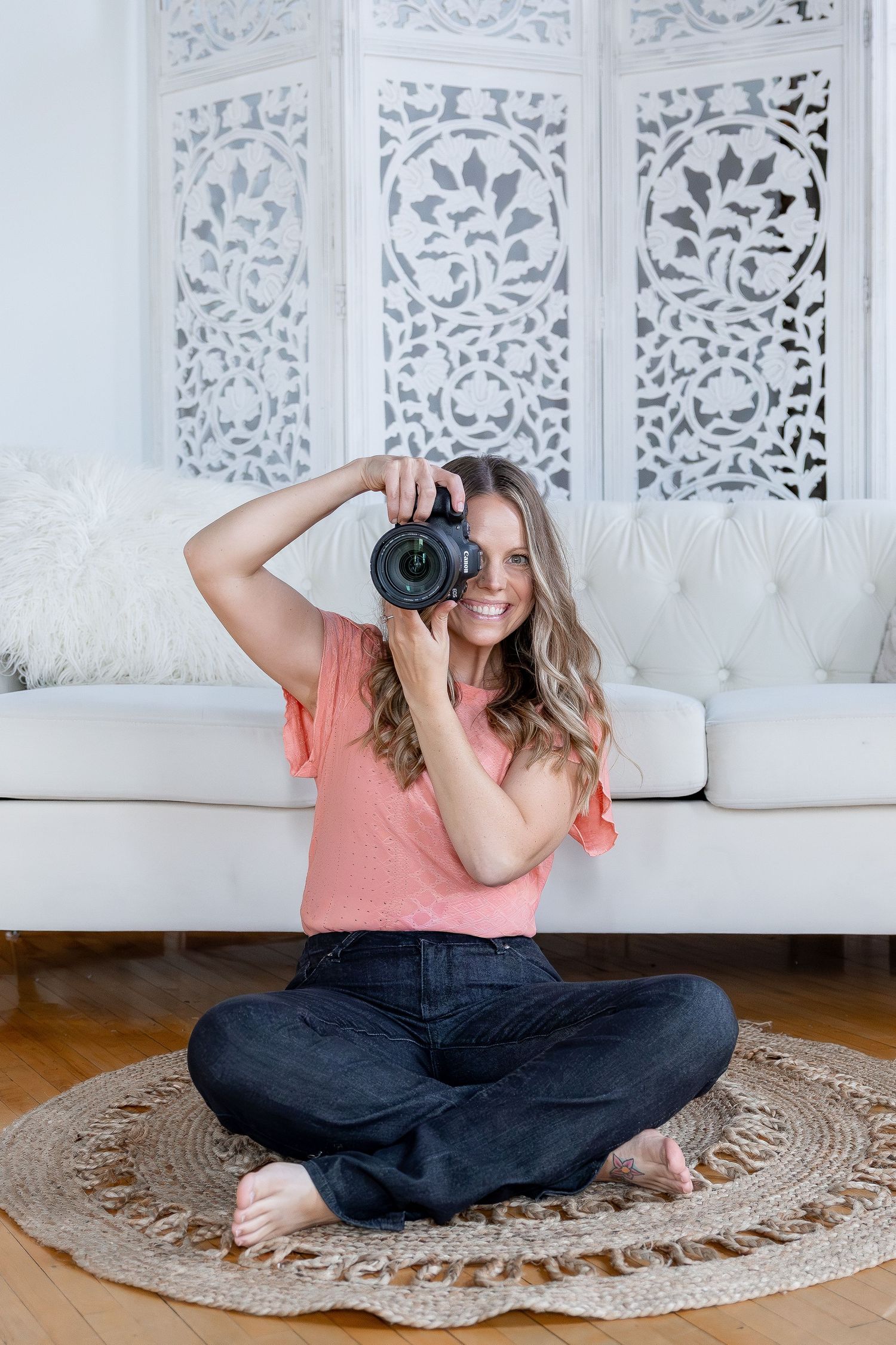 Photographer in pink shirt taking pictures while sitting on round rug.