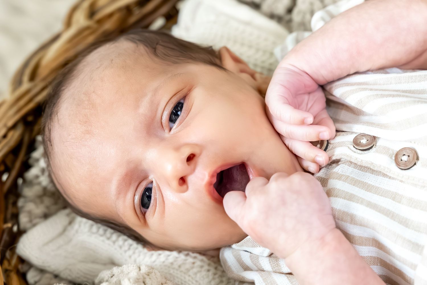 Baby wearing pink and white striped outfit lying on textured surface during photo session.