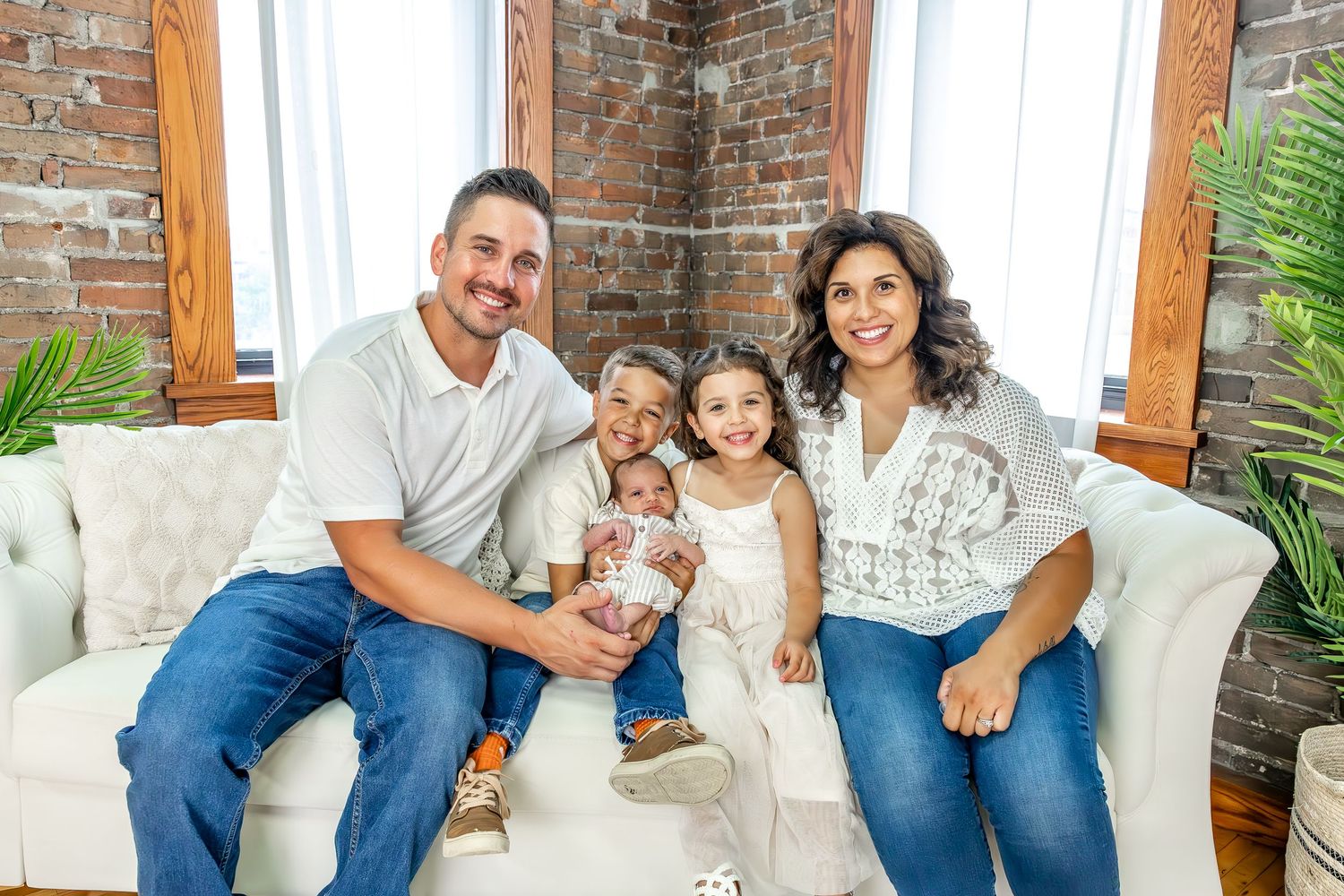 A family relaxes together on a white tufted sofa in a room with exposed brick walls.