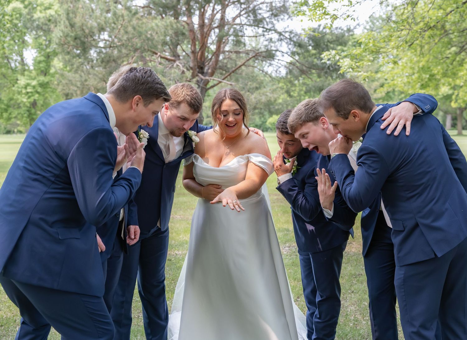 Wedding party in navy blue suits and white dress laughing together in outdoor garden setting.