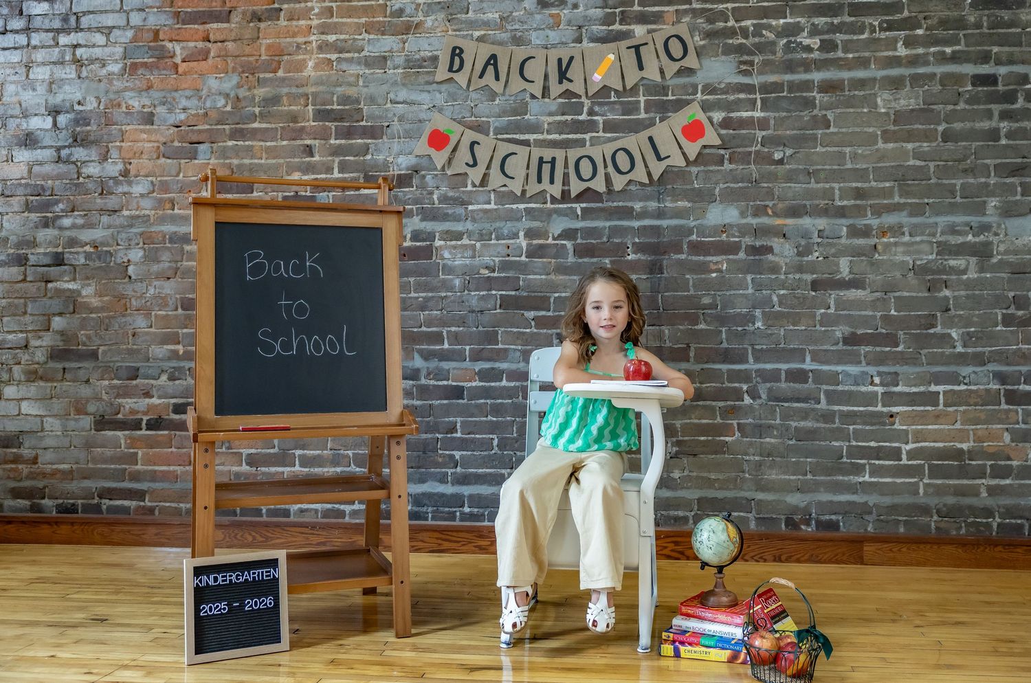 Back to school setup with chalkboard, books, and decorative banner against brick wall background.