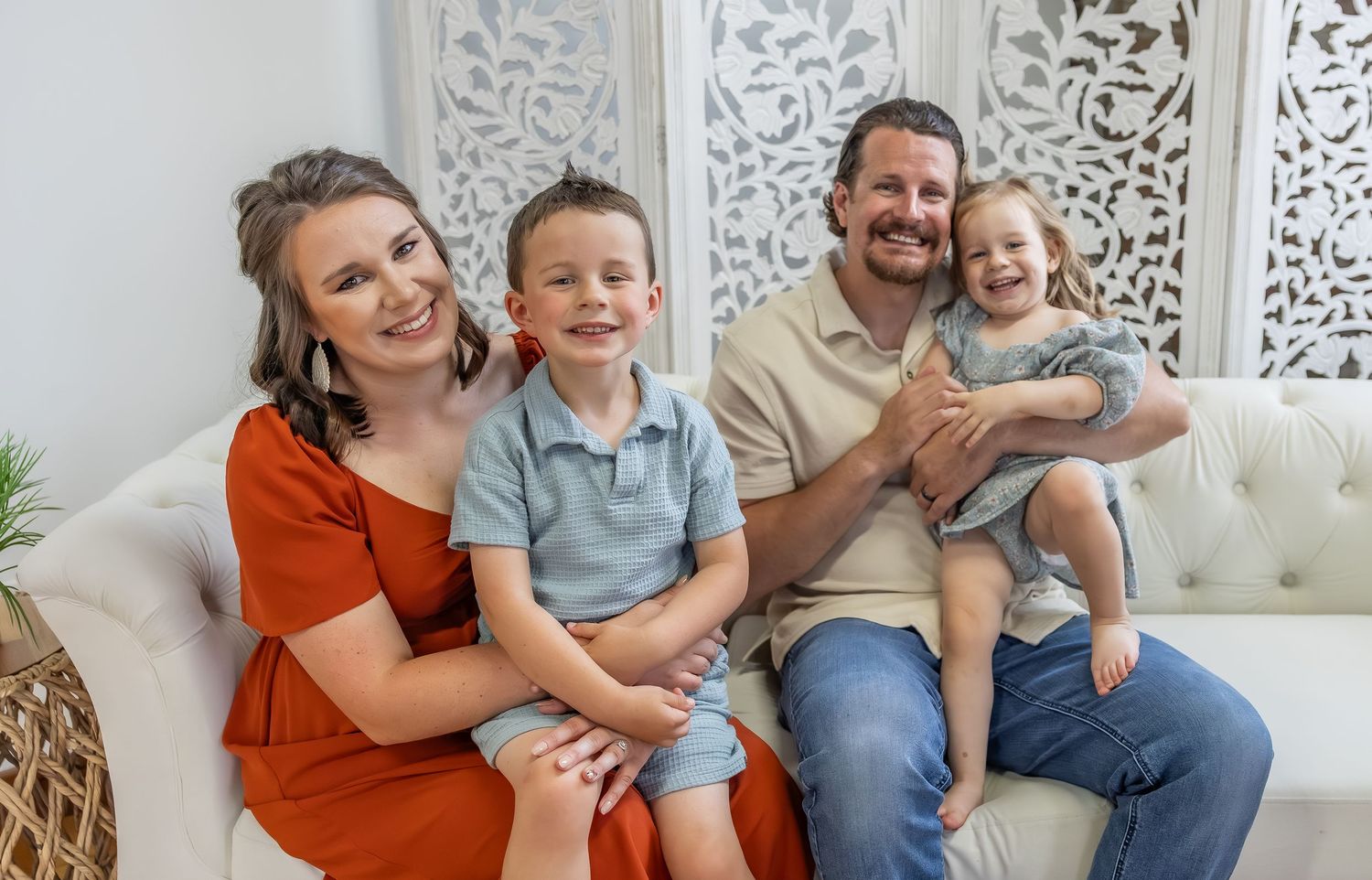 Happy family portrait session on white couch with decorative wall backdrop.