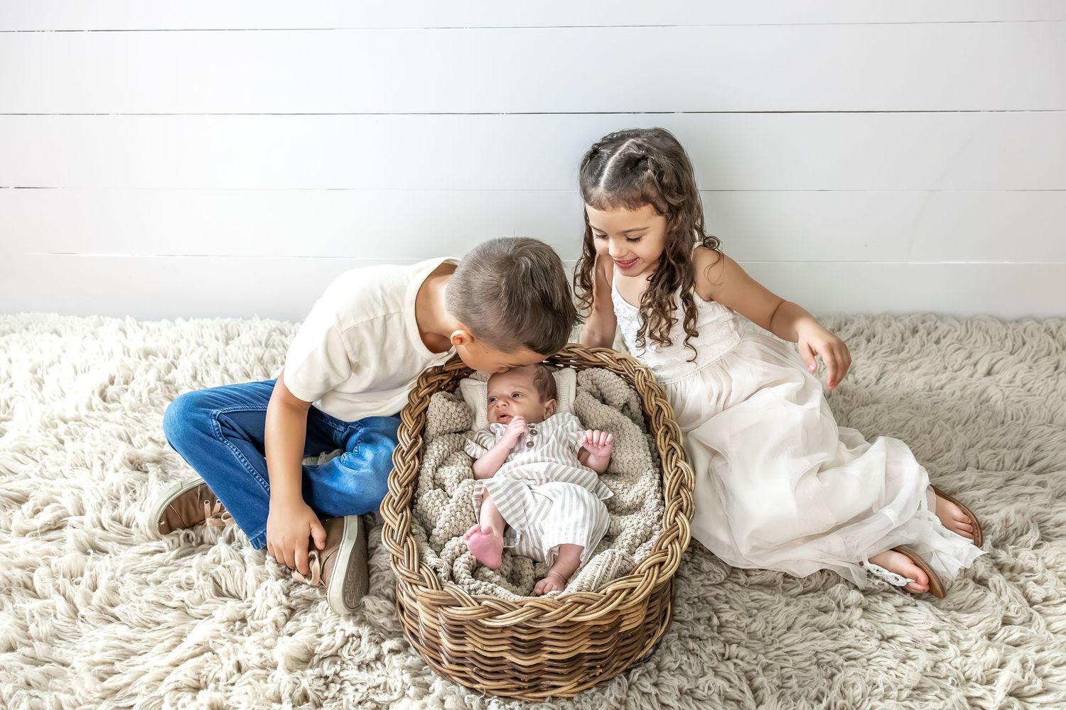 Family gathered around woven basket during indoor photo session on white floor.