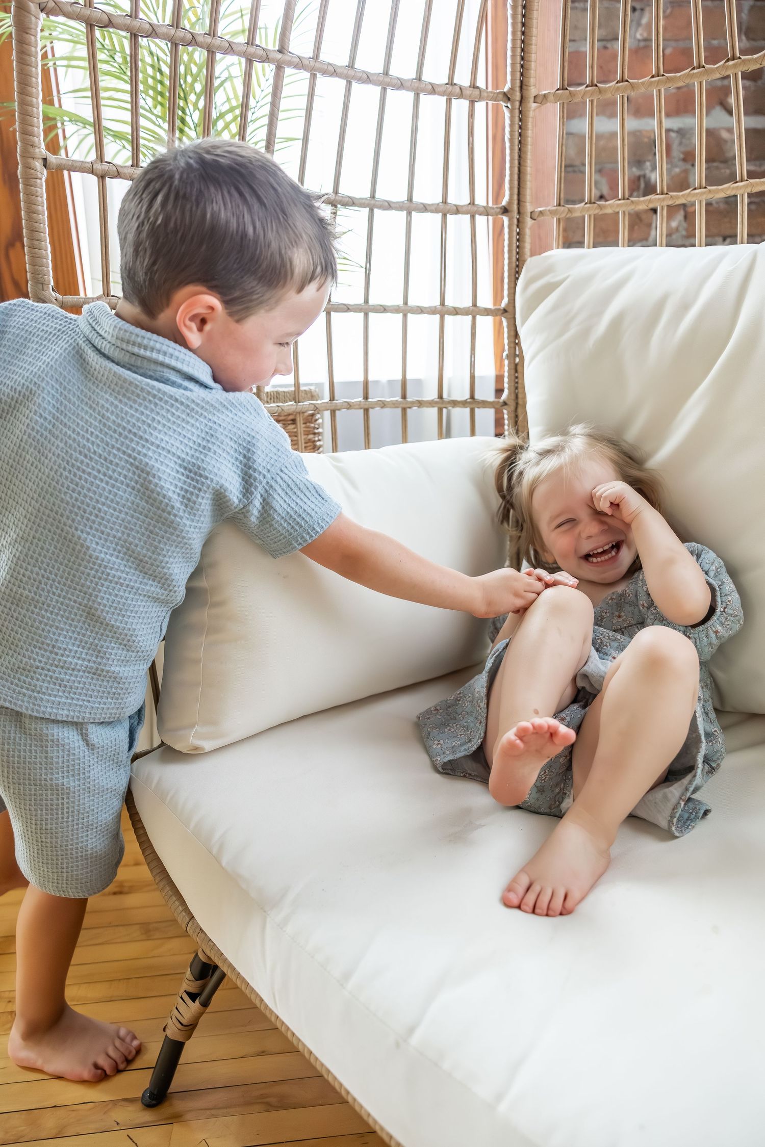 Two playful children on a white couch share a joyful moment together.