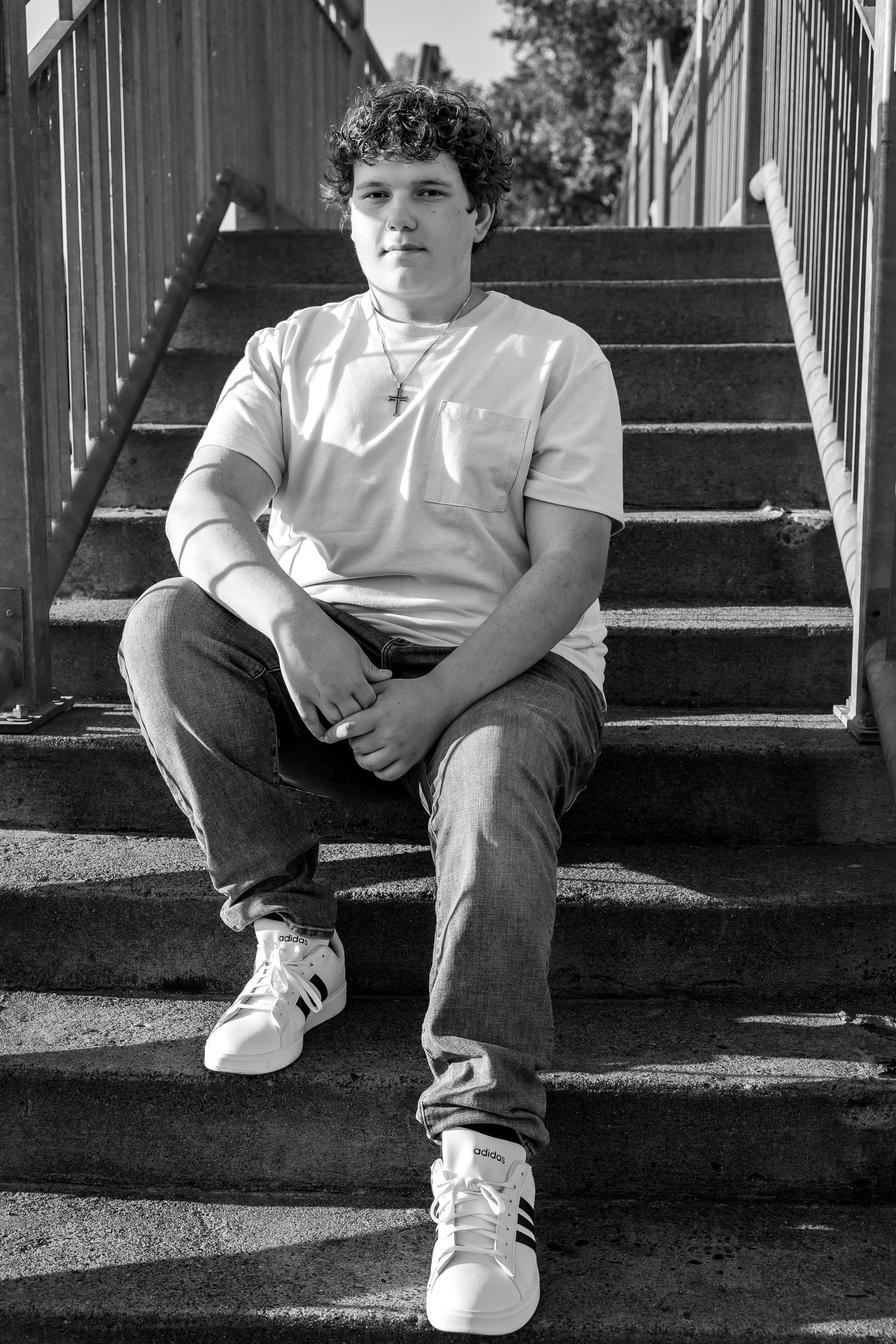 Black and white portrait seated on concrete stairs wearing casual attire and white sneakers.