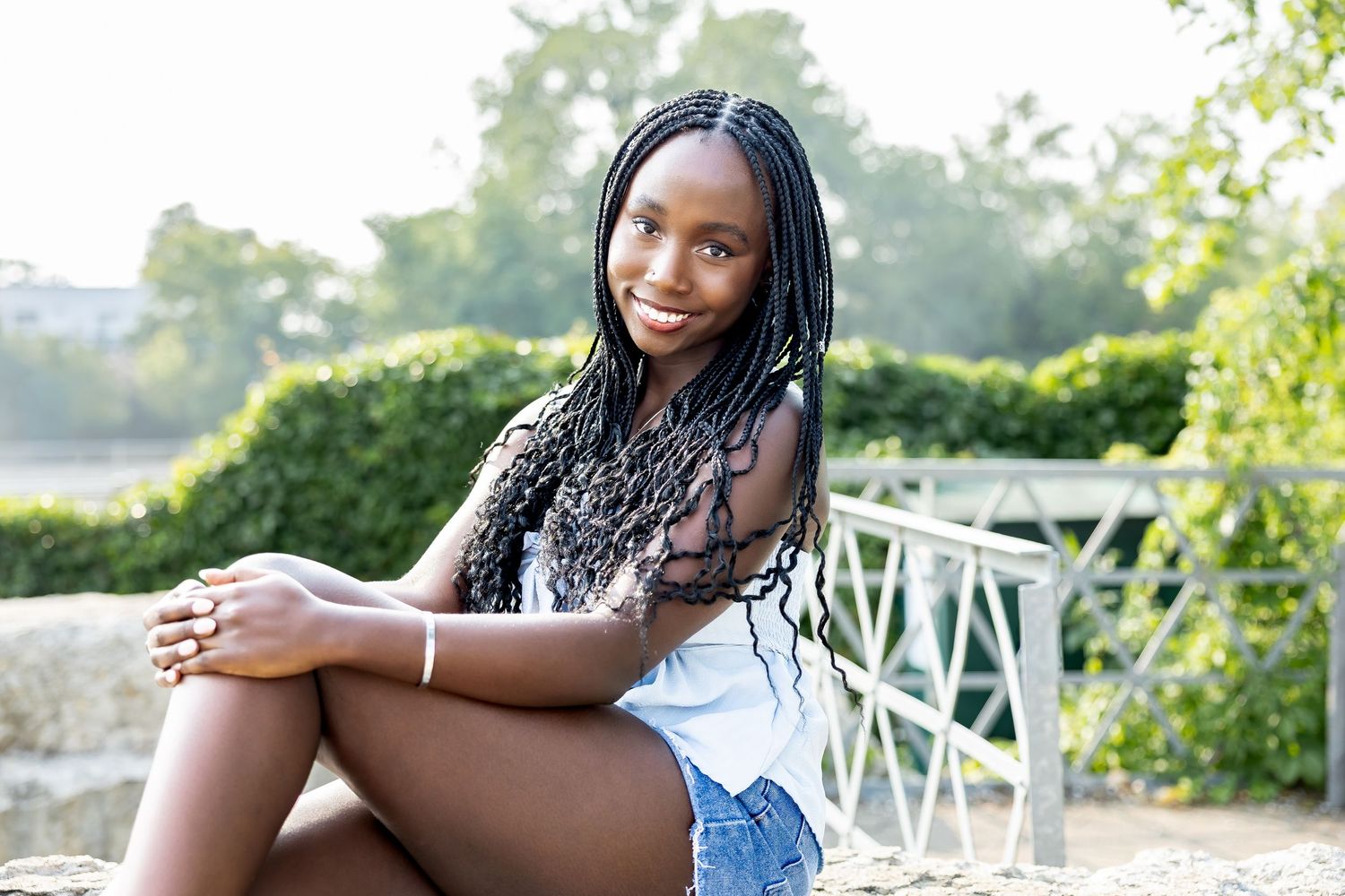 A person poses gracefully on a white railing during an outdoor photo shoot.
