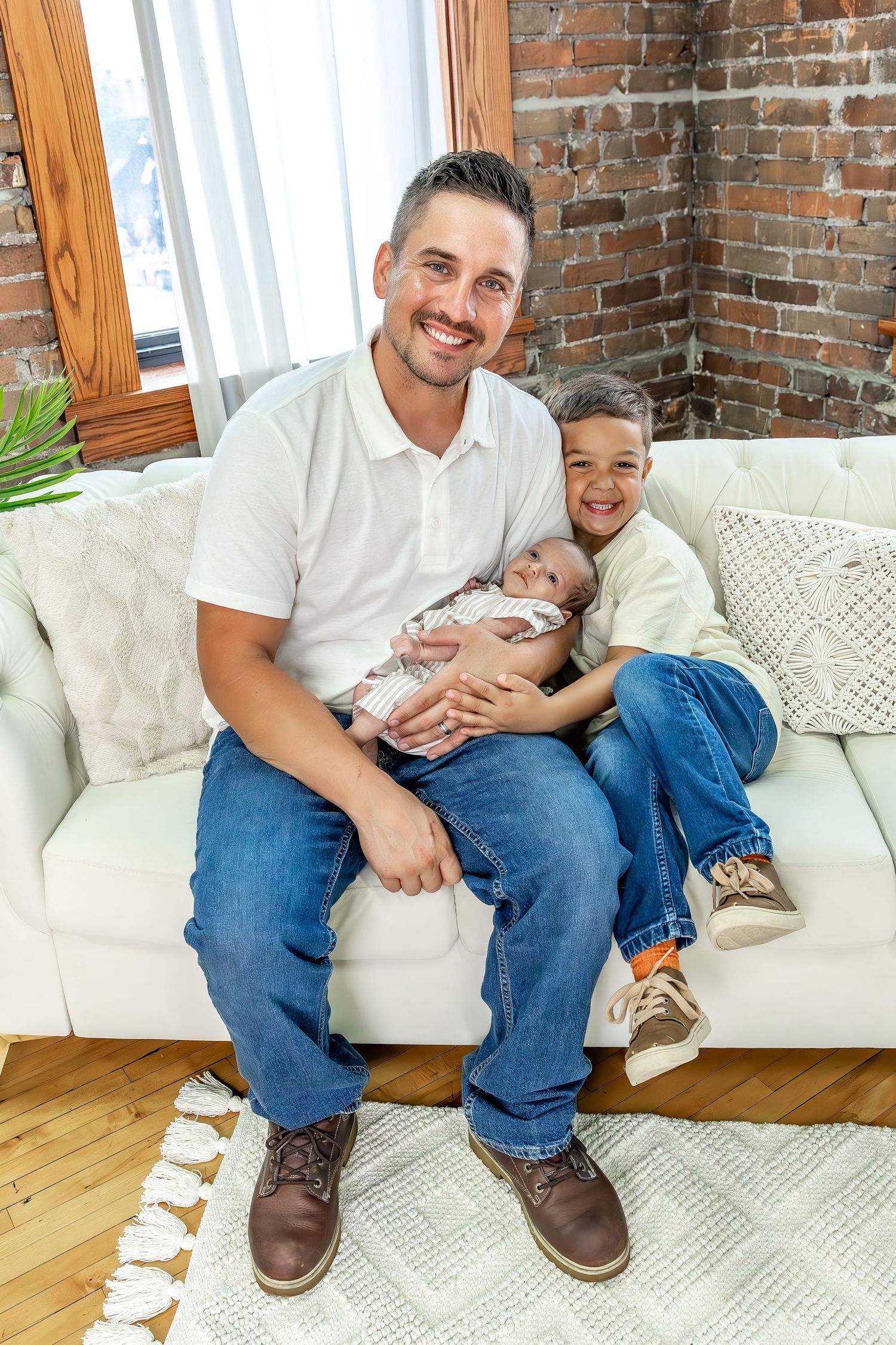A family shares intimate moments while sitting on a white sofa with exposed brick walls.
