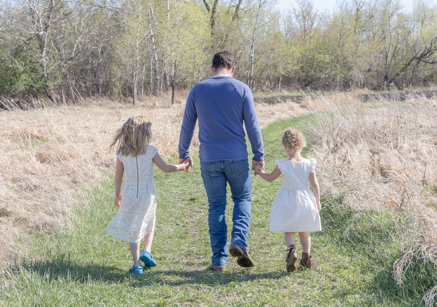 Family walking together on a grassy trail surrounded by spring foliage.